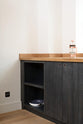 A quiet corner of a simple and contemporary Sebastian Cox kitchen features a long sink and cooker run with a solid oak worktop. Adorned with a copper coffee press, a white pan, and copper pull rings, this kitchen creates a cosy space with industrial details and a practical finish.