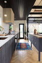 Nestled between a large and minimal Sebastian Cox kitchen, which features a long sink and cooker run with a Carrara marble worktop and a large kitchen island with a solid oak worktop, is a slim glass door leading to the gorgeous countryside of Tuscany. Beautifully decorated with artisan ceramics, a large cactus plant, a wicker basket, and a bright patterned rug, this kitchen creates a simple and practical space.