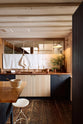 A warm and stylish Sebastian Cox kitchen features a sink run with two single copper sinks, aged brass Mayan taps, glazed partitions, a copper worktop, and a prep table with a solid oak worktop. Adorned with an aged brass café curtain rail, a milk glass task light, artisan ceramics, and vintage wooden items, this kitchen creates a humble space that celebrates a love of simple and natural materials.