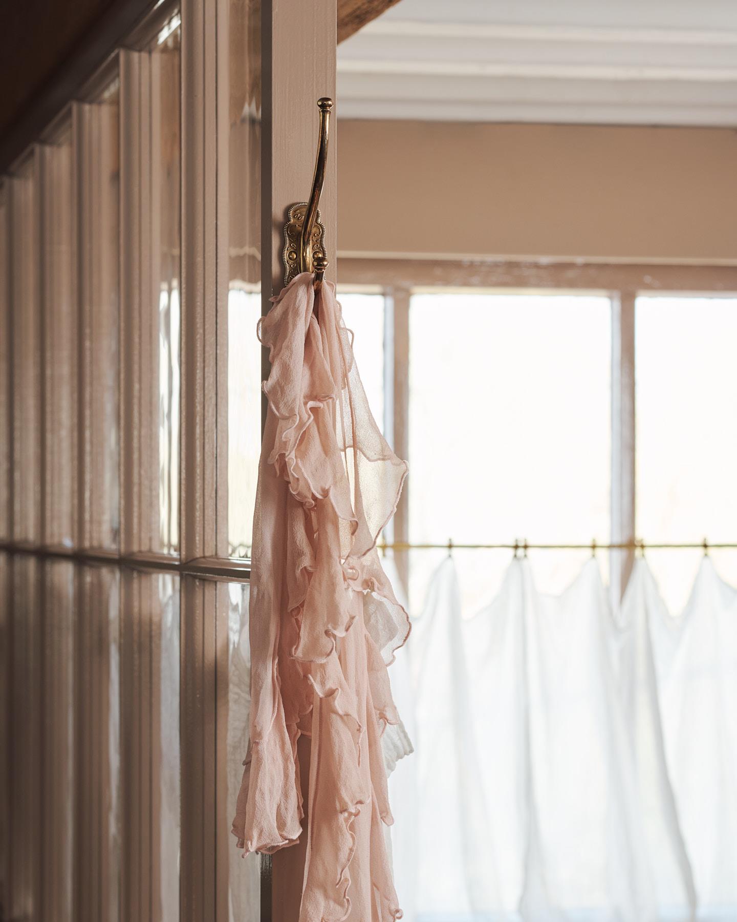 A small Parisian café-style brass hook, fitted to the frame of a pink painted glazed partition with a lovely pink frilled scarf draped on it.