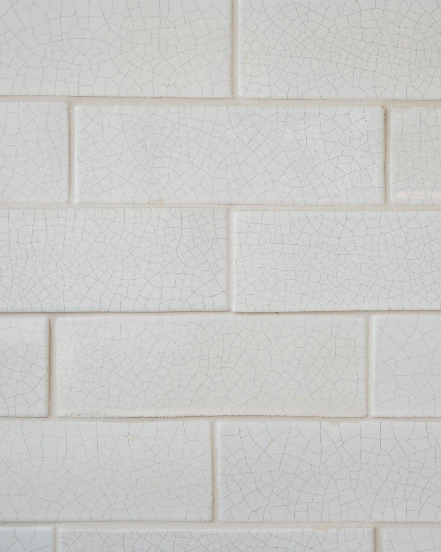 A close-up view of glossy white metro wall tiles with delicate charcoal crazing across the surface.