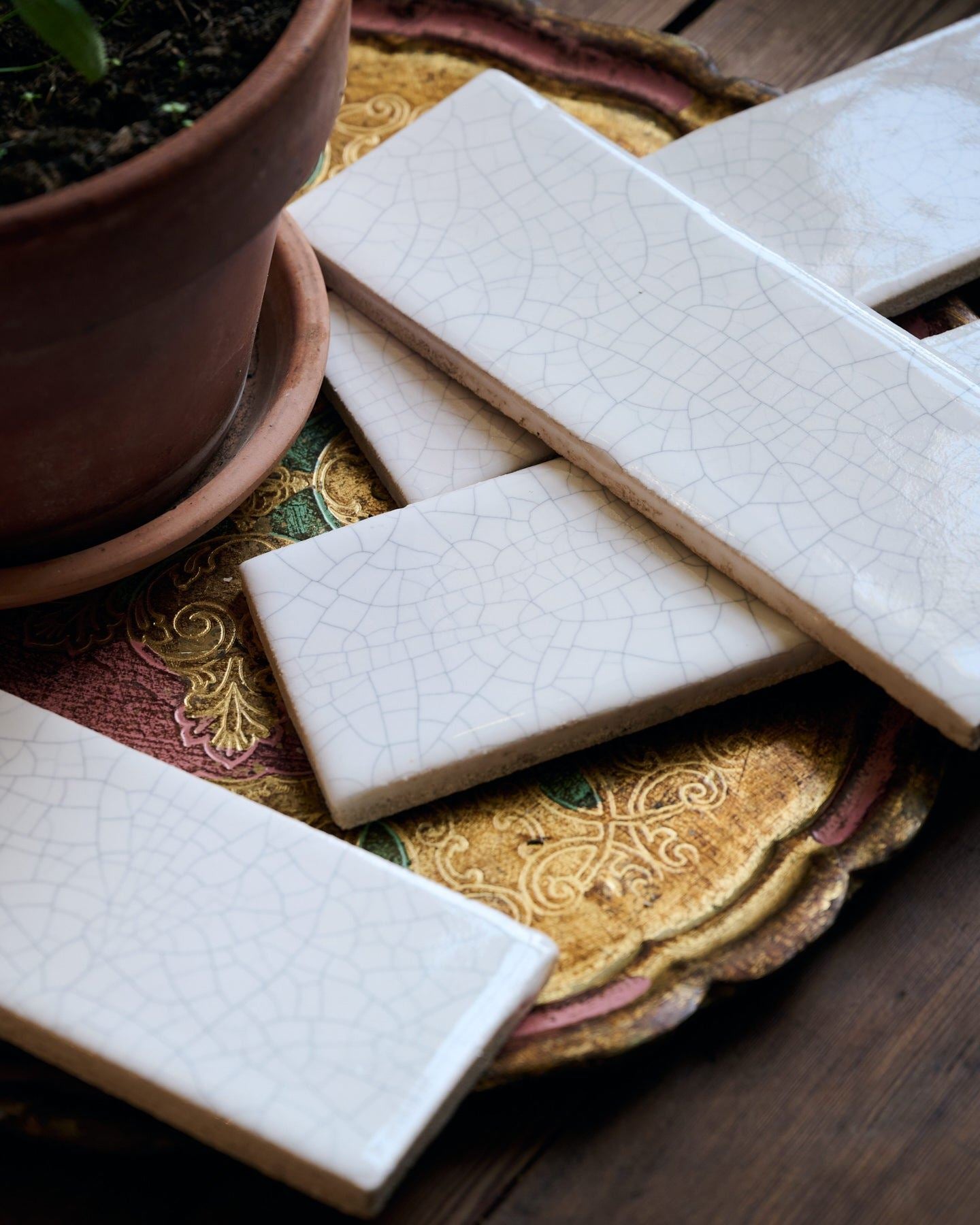 Several white glossy metro tiles on a decorative brass plate, each tile has unique delicate crazing across the surface.