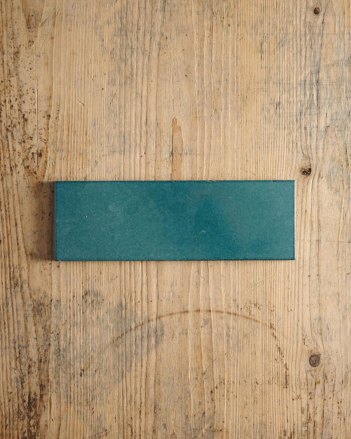 A glossy teal wide metro tile on a rustic wooden surface. | Plain Long Metro TEST