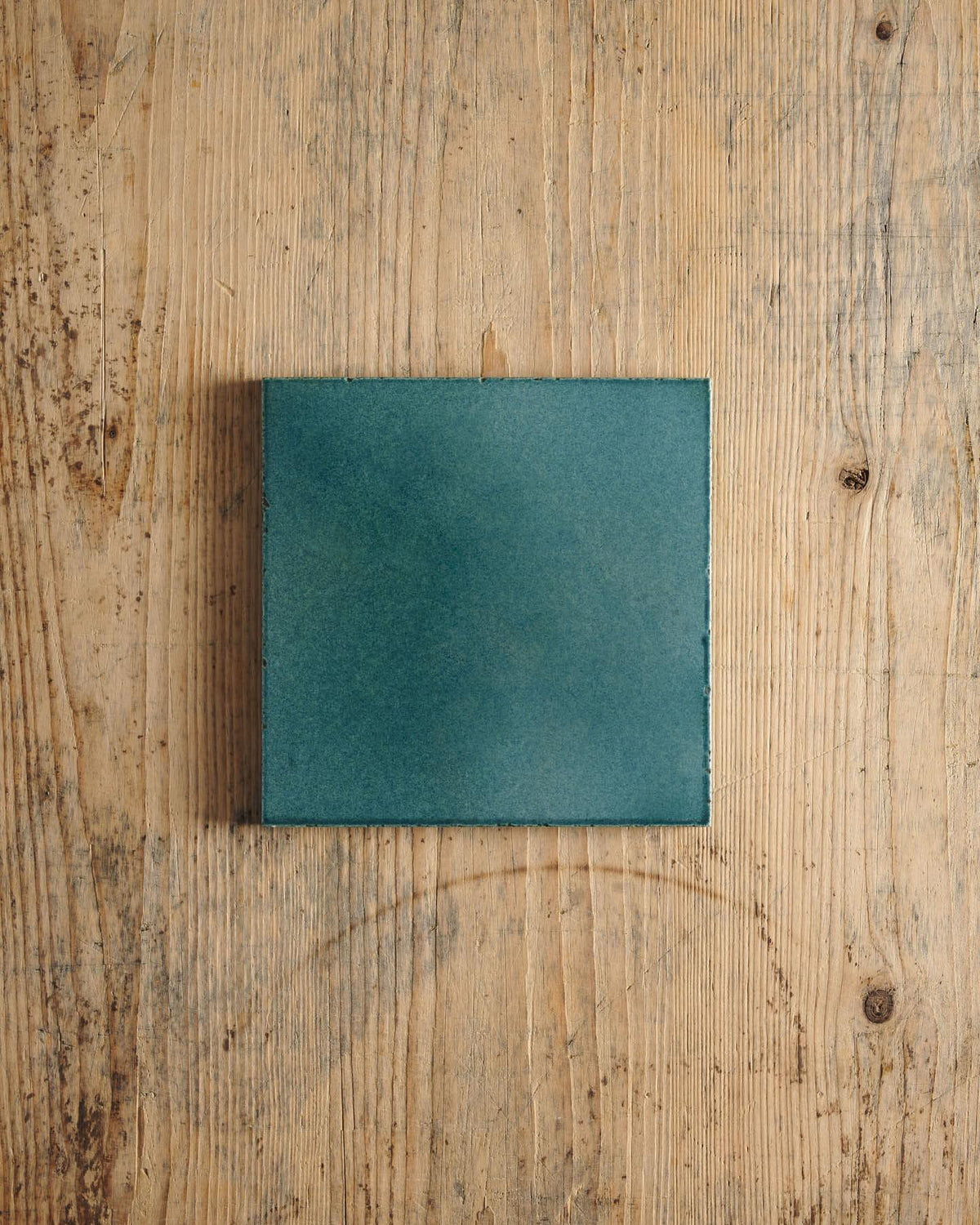 A glossy teal square tile on a rustic wooden surface. | Plain Square TEST
