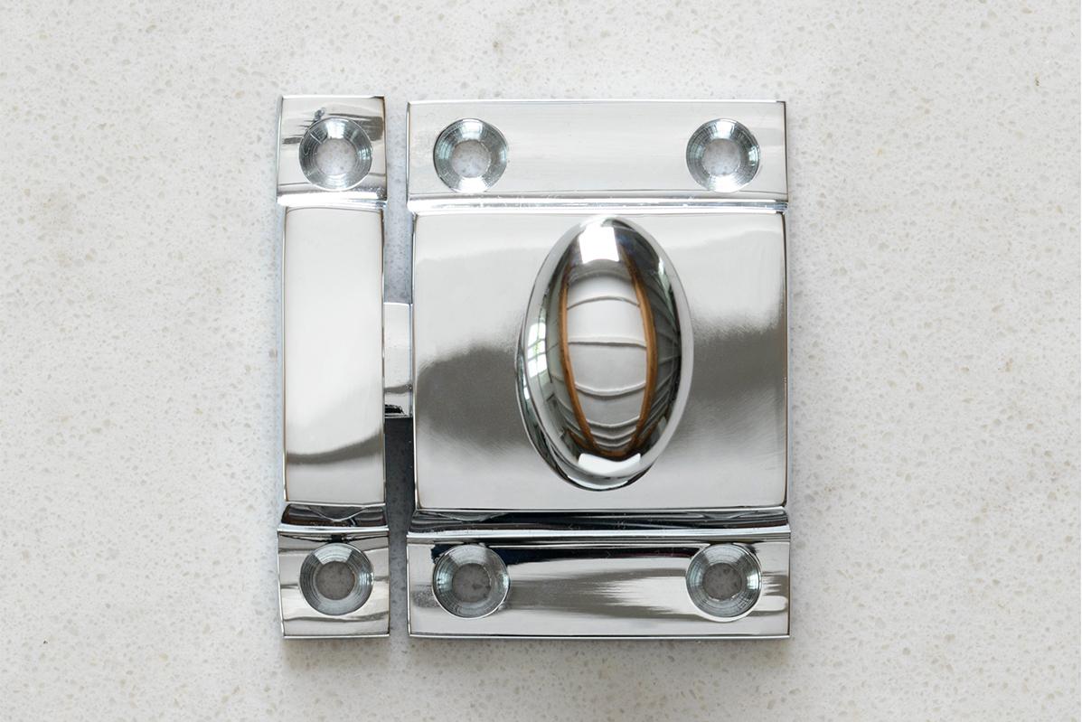 A square cupboard catch with an oval-shaped knob in a polished 'Bella' chrome finish.