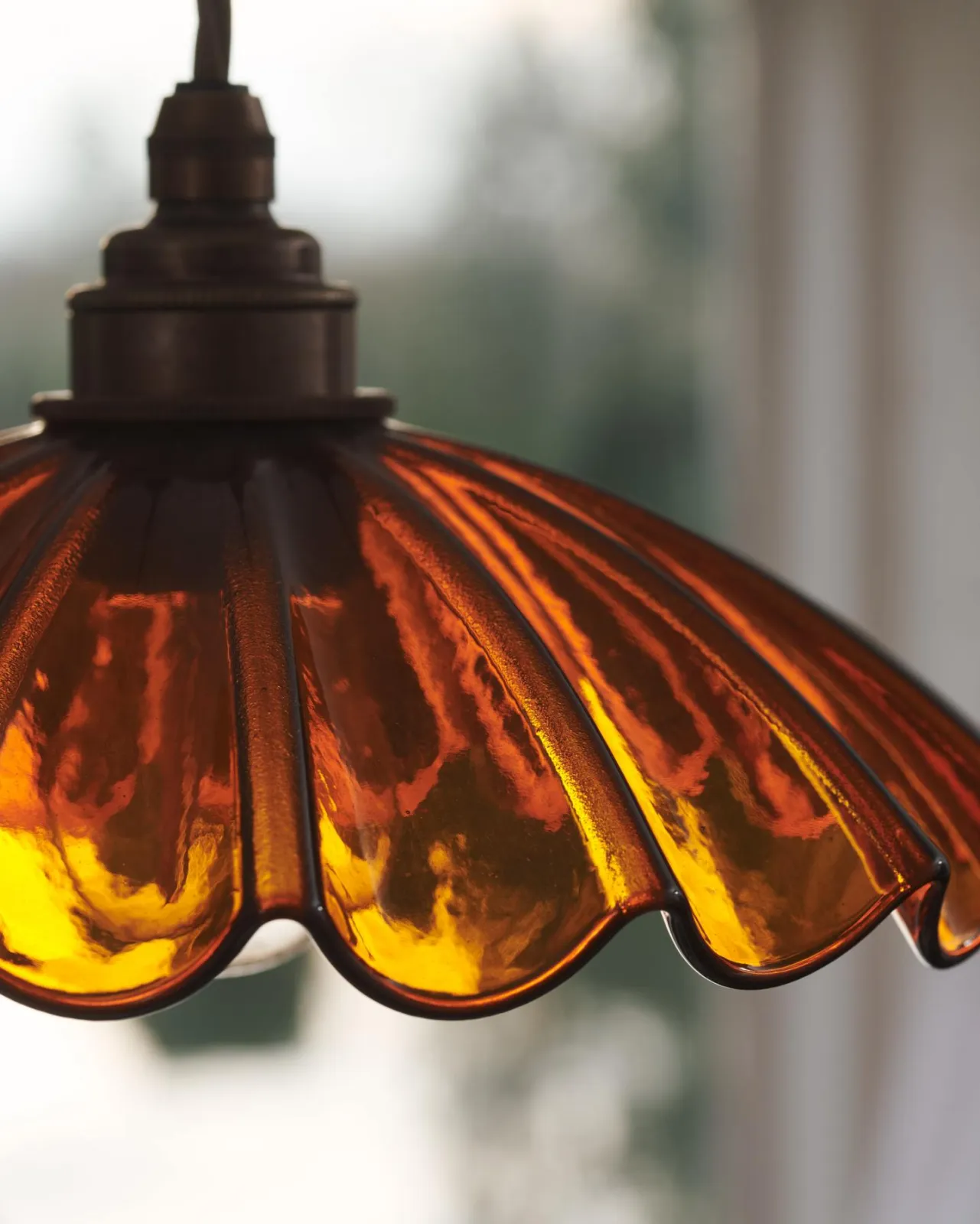 A close-up view of a small frilly amber glass light shade. Light from a window behind is shining through the translucent glass.