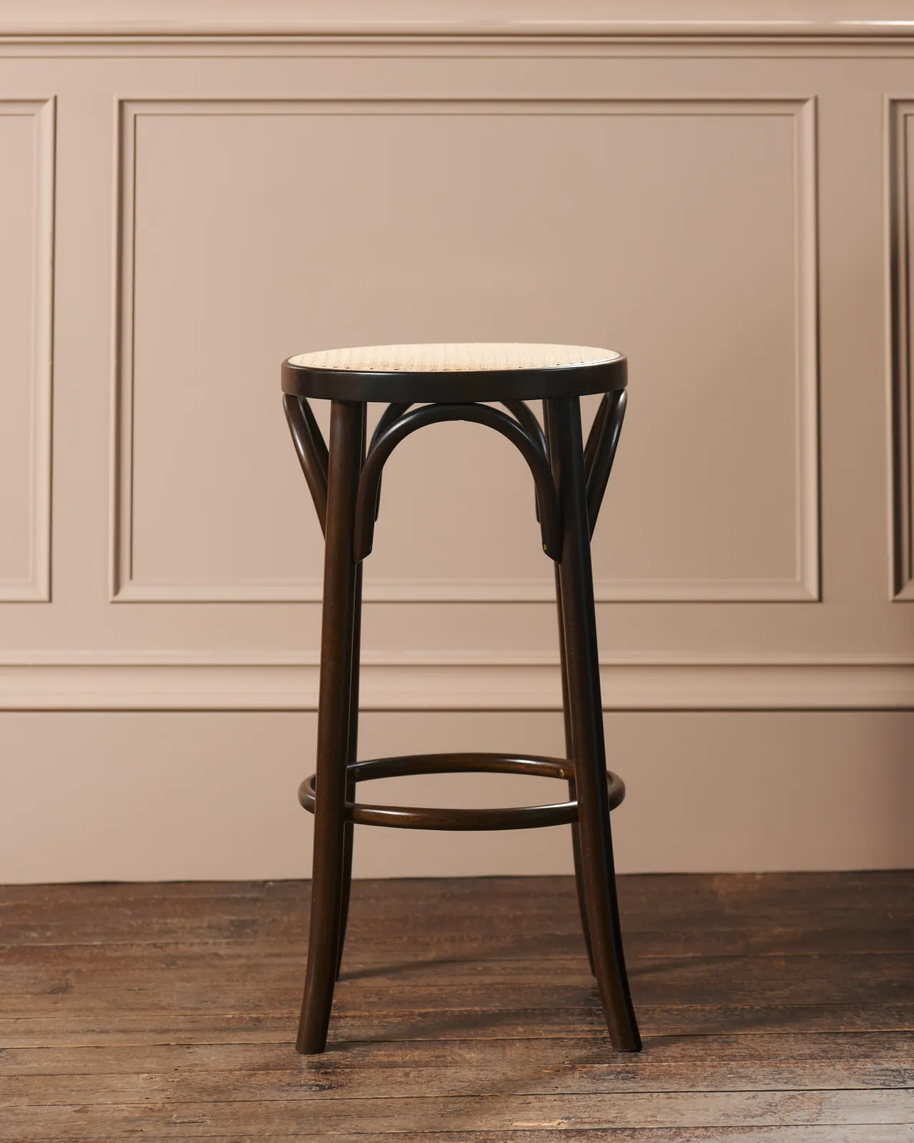 A front profile view of a café-style bar stool with a dark stained frame and light woven ratten seat.