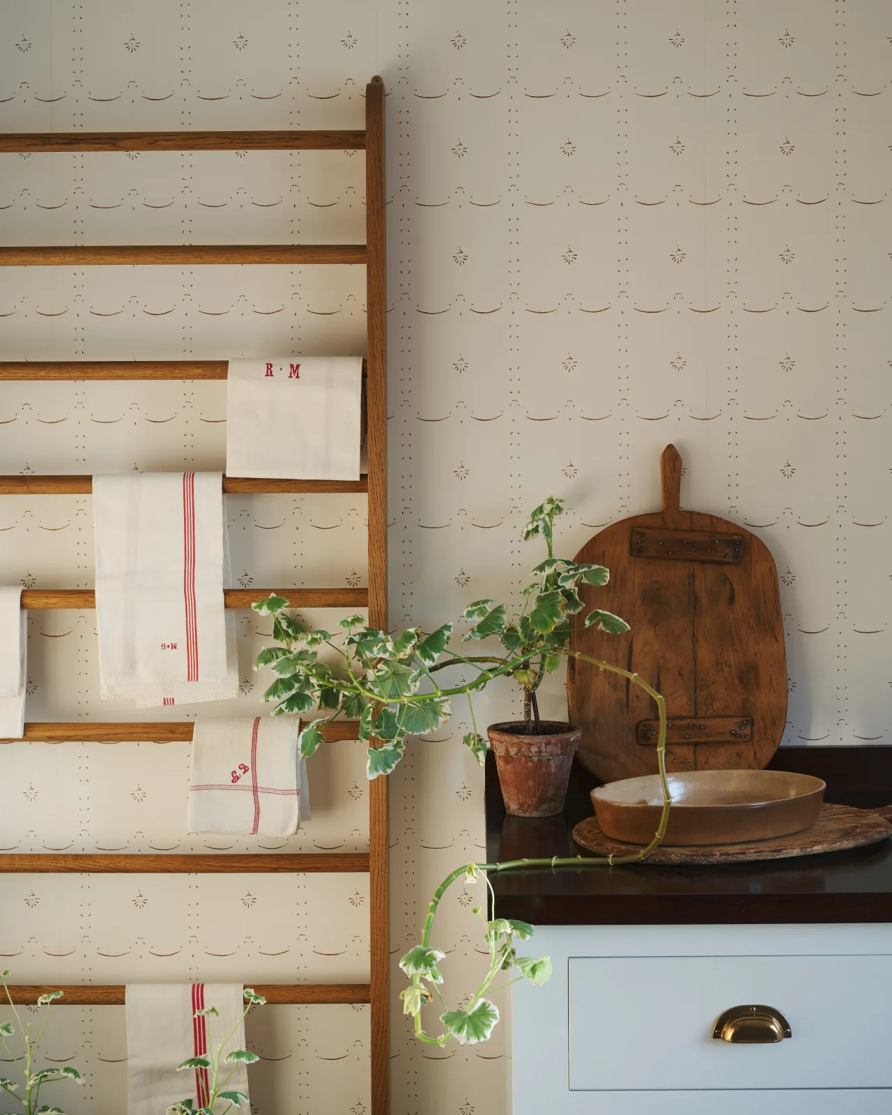 A delicately patterned wallpaper behind a mid-century-style oak hanging rack.