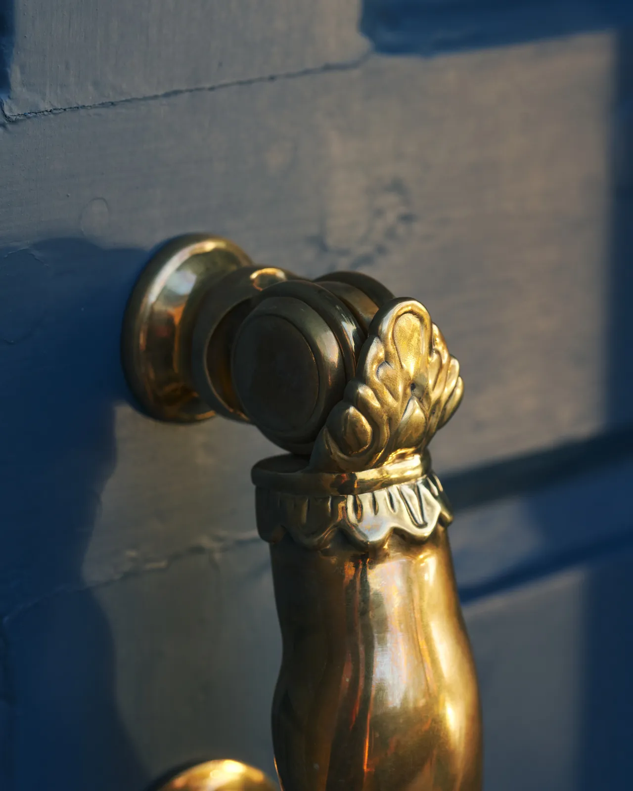 A close-up view showing the hinged part of a decorative brass door knocker with traditional details.