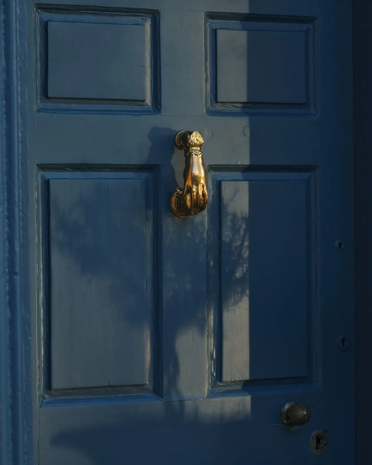 An oblique view of a decorative brass door knocker, shaped like a hand holding a pomegranate and fitted to a blue painted door.