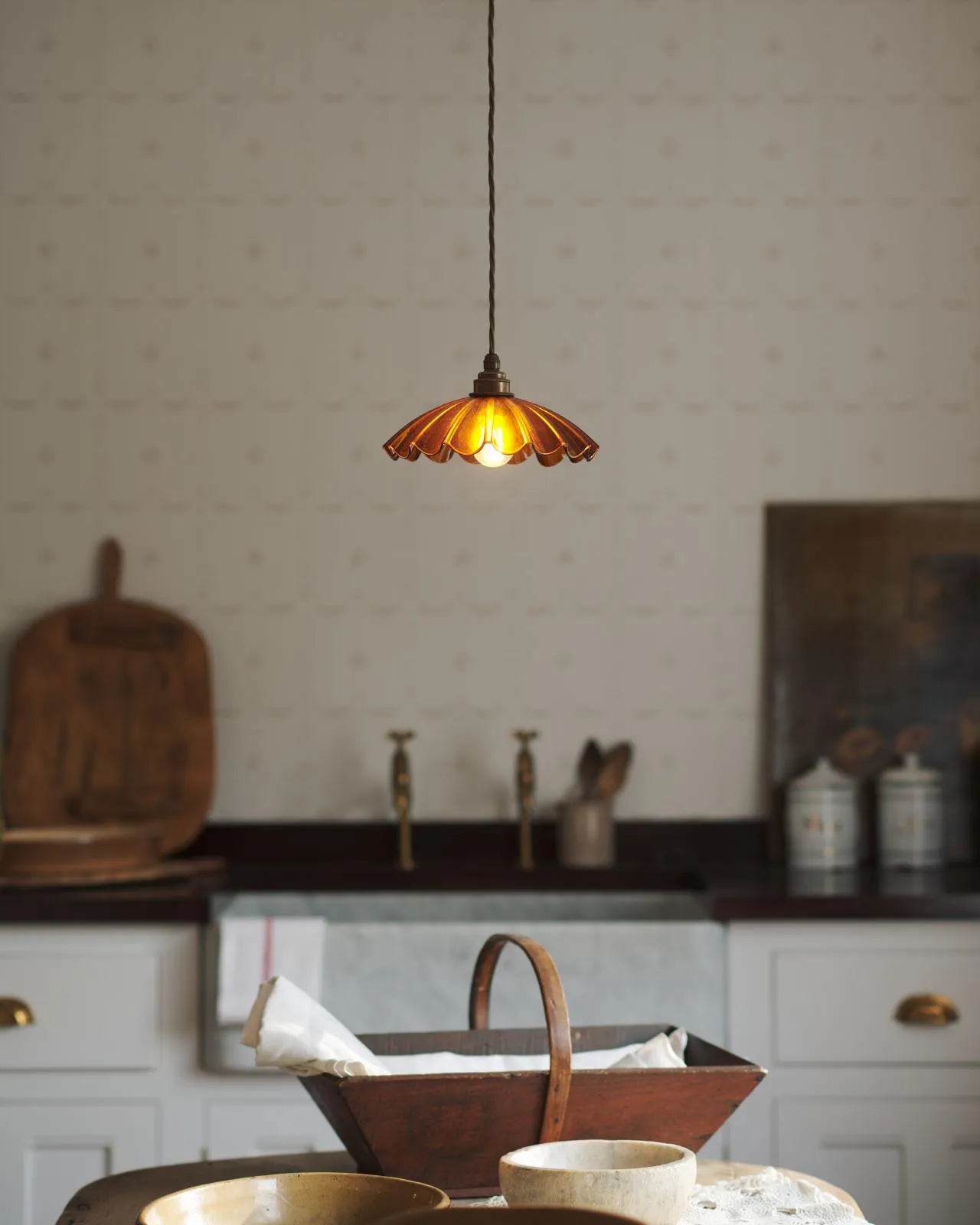 A small frilly amber glass pendant light with brass fittings and brown twisted fabric flex cord. The light is on and shining through the tranlucent glass.