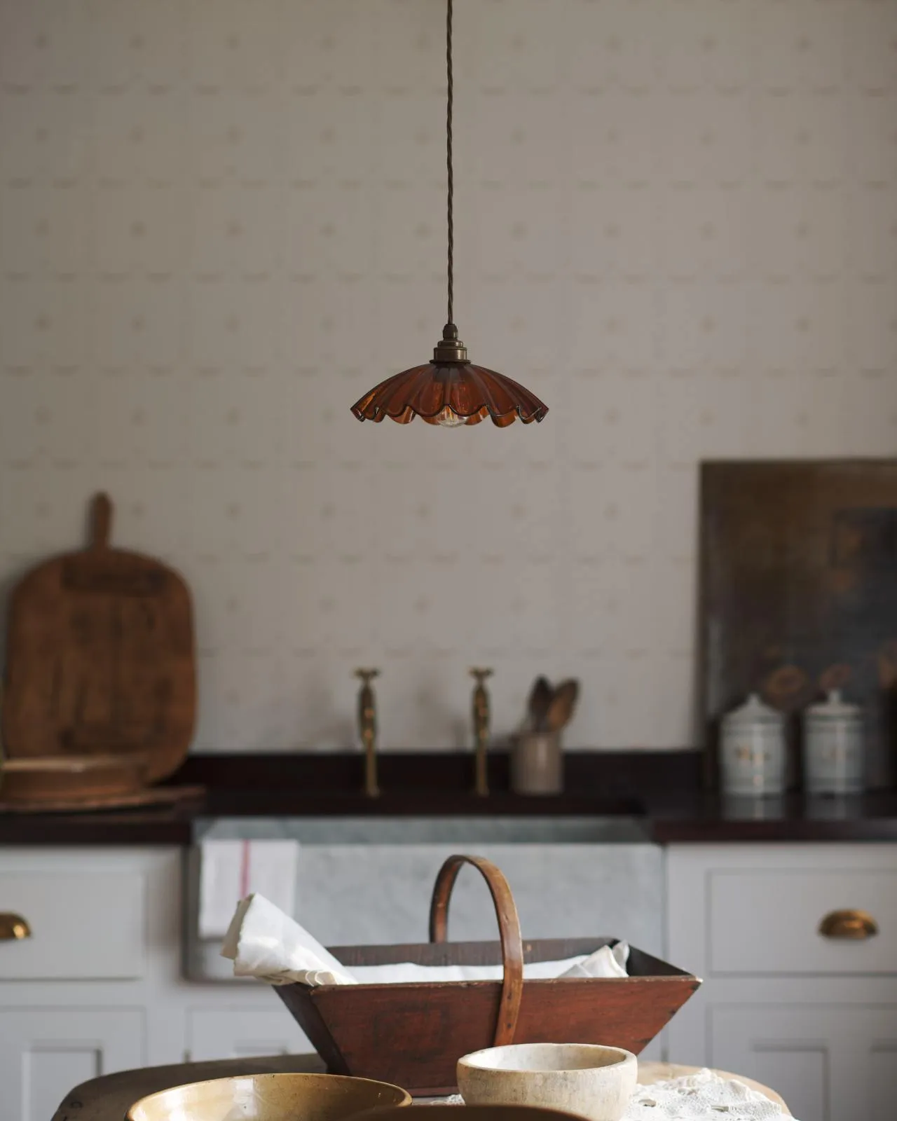 A small frilly amber glass pendant light with brass fittings and brown twisted fabric flex cord. The light is off.