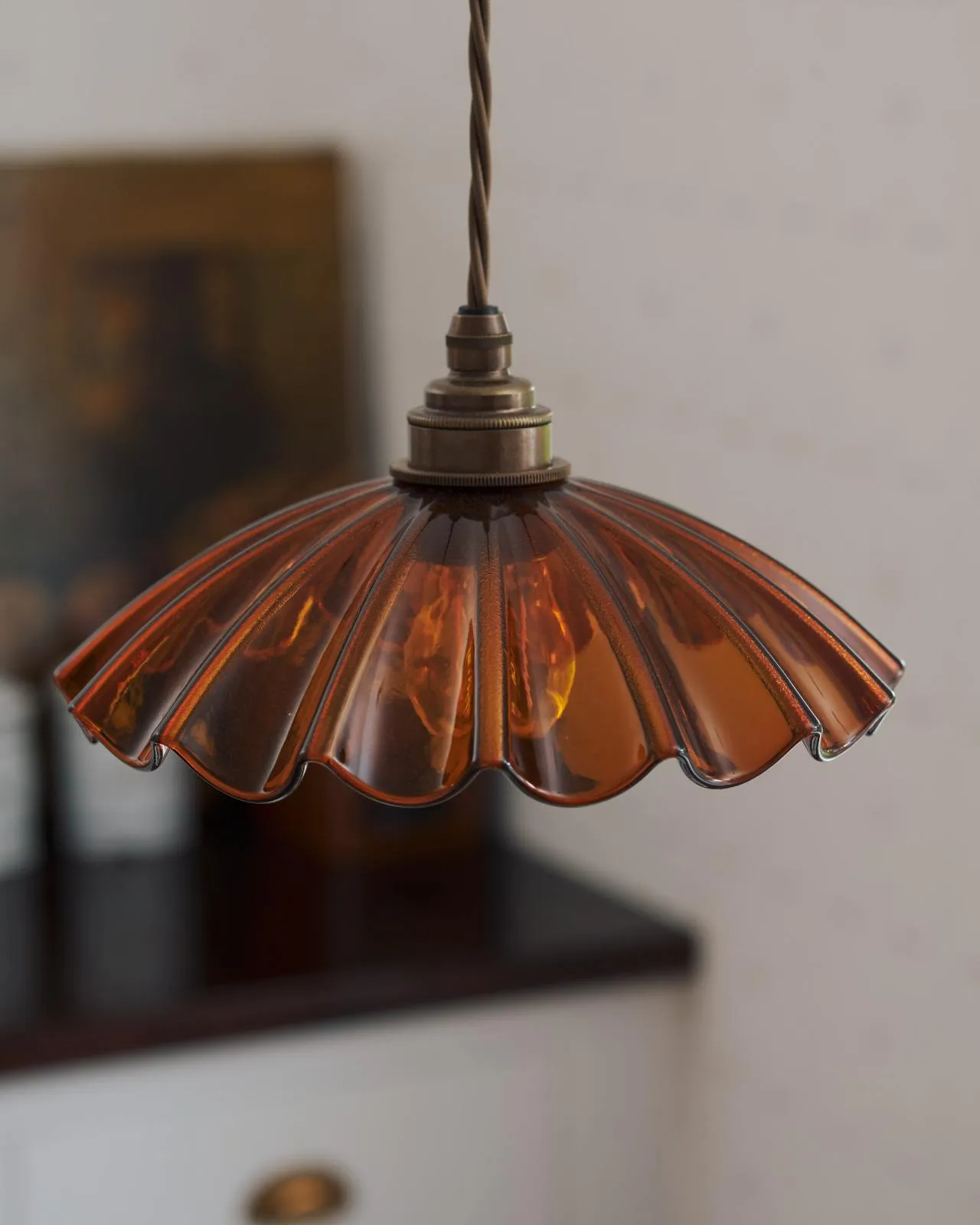 A close-up oblique view of a small frilly amber glass light shade with brass fittings and brown twisted fabric flex cord.