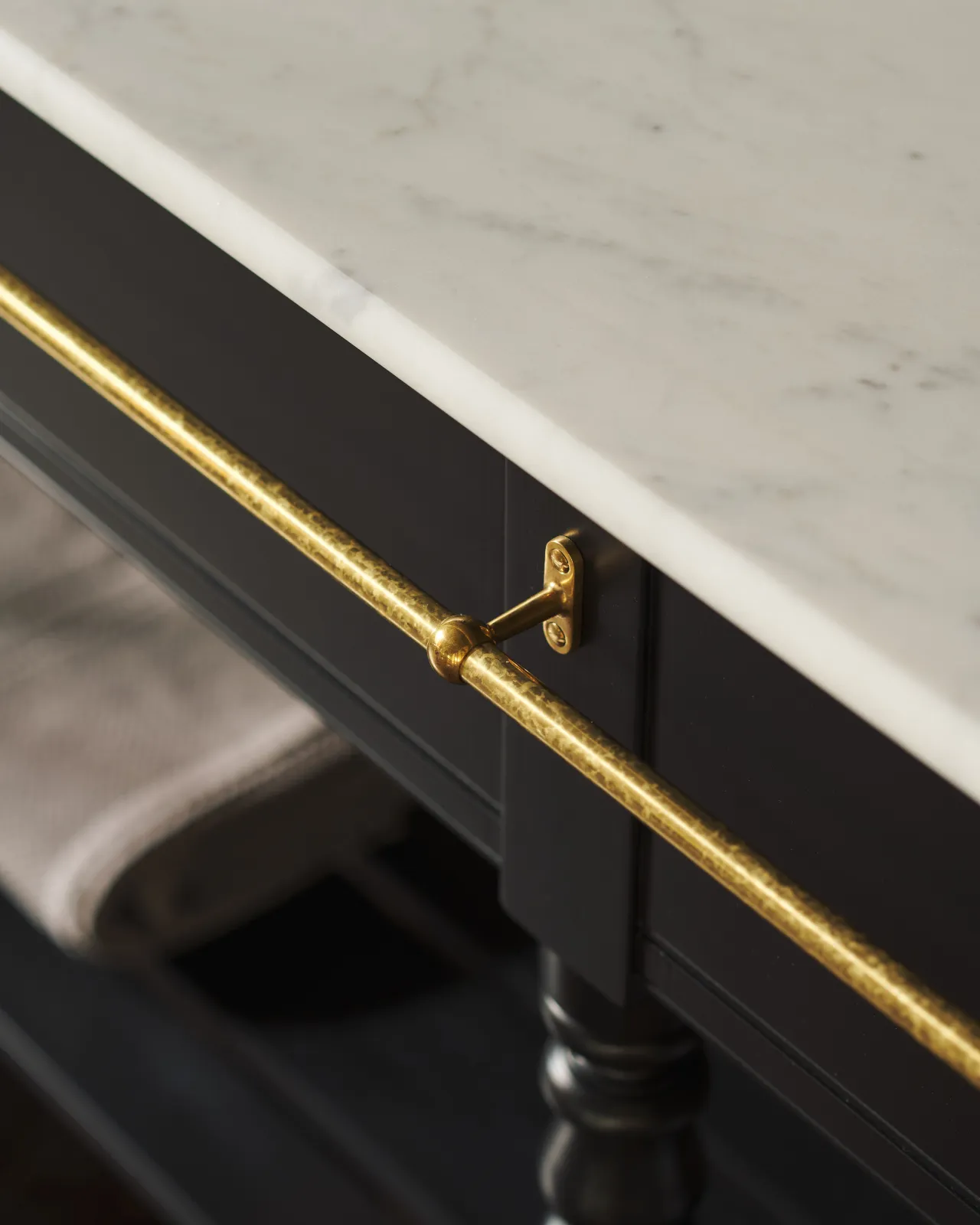 A detailed view of an aged brass towel rail attached to the front of a Victorian-inspired washstand.