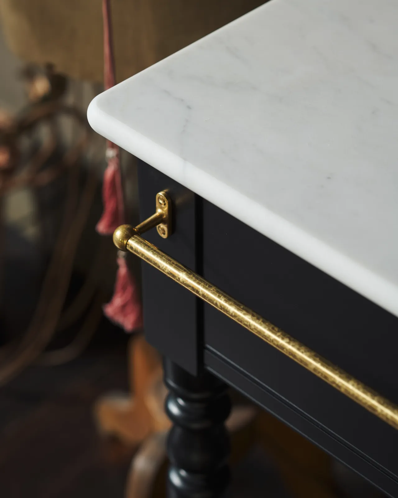 A detailed view of an aged brass towel rail attached to the front of a Victorian-inspired washstand.
