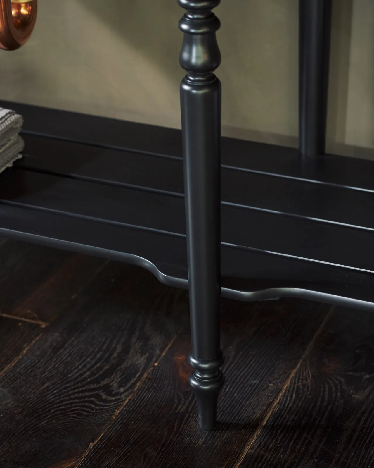 A close-up view of a black painted slatted shelf at the base of a Victorian-inspired washstand.