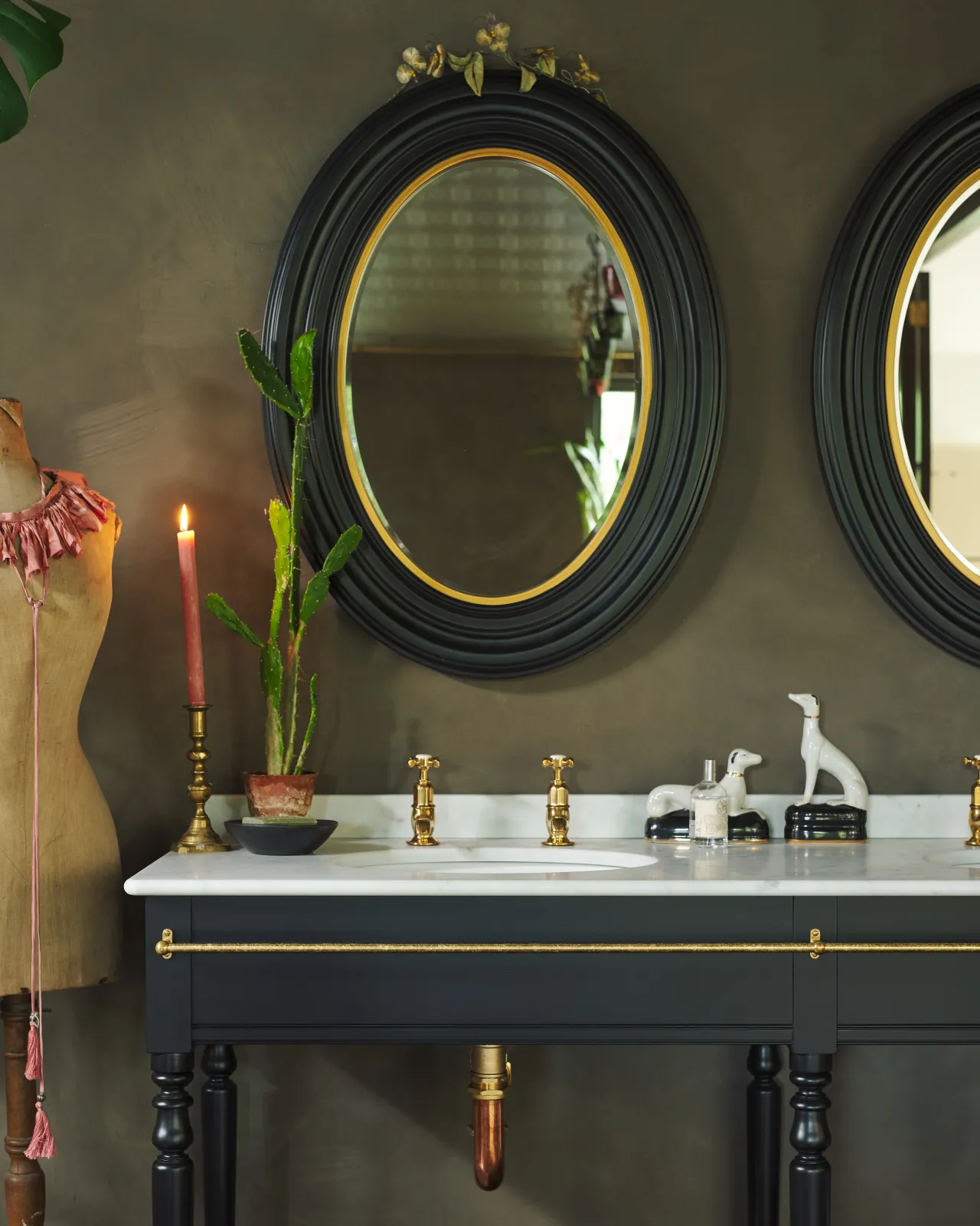 A straight-on view of a black Victorian-inspired washstand with a Carrara marble worktop, brass pillar taps, a copper p-trap and an aged brass towel rail attached to the front.