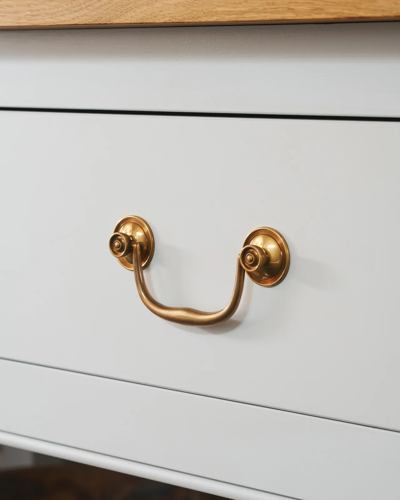 An angled view of an elegant Georgian-style brass swing handle for kitchen cupboard drawers.