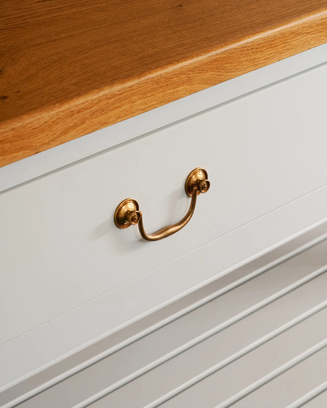 Two Georgian-style brass swing handles on a large light-coloured Shaker-style kitchen prep table with a warm oak worktop.