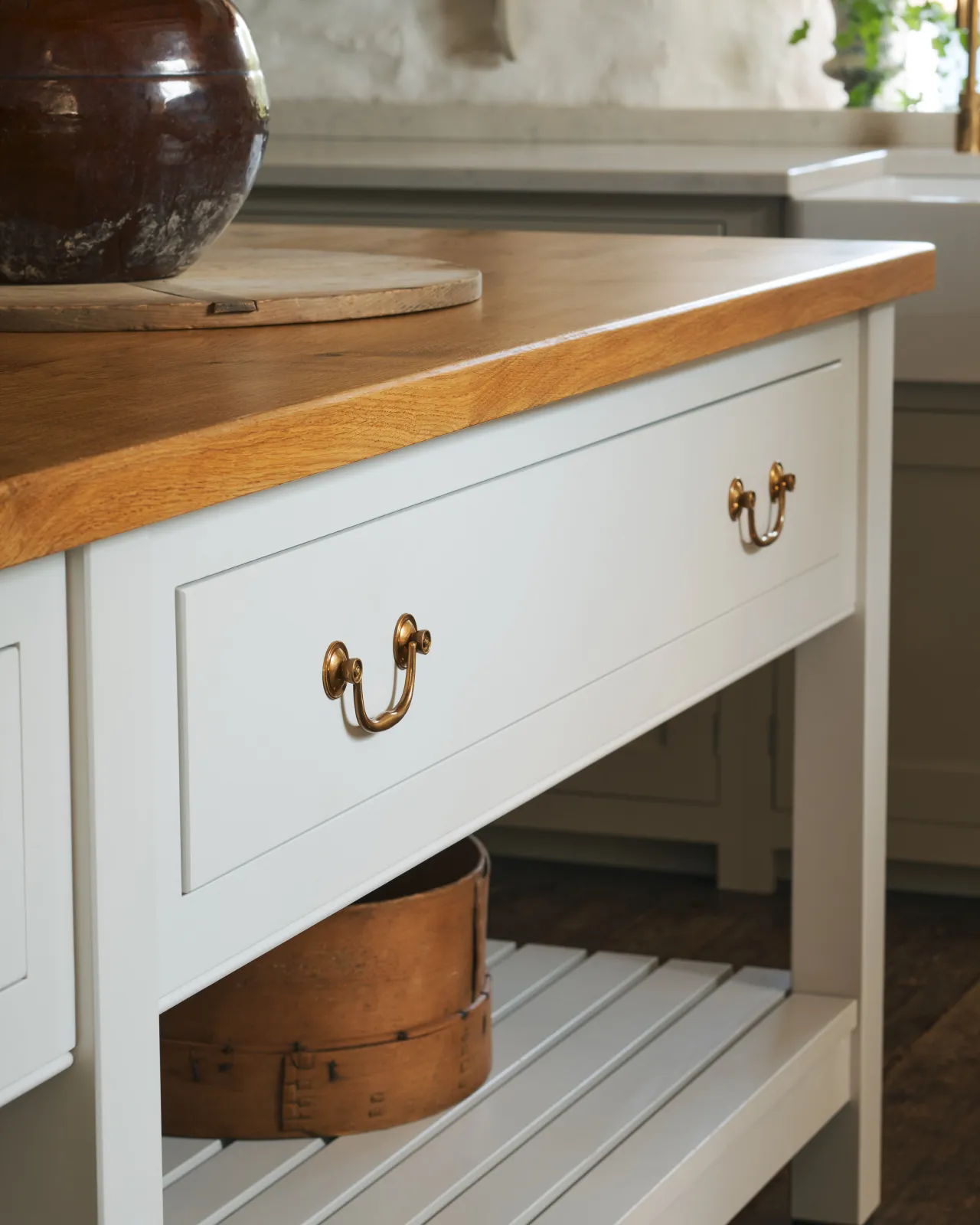 Two Georgian-style brass swing handles on a light-coloured Shaker-style kitchen prep table with a warm oak worktop.