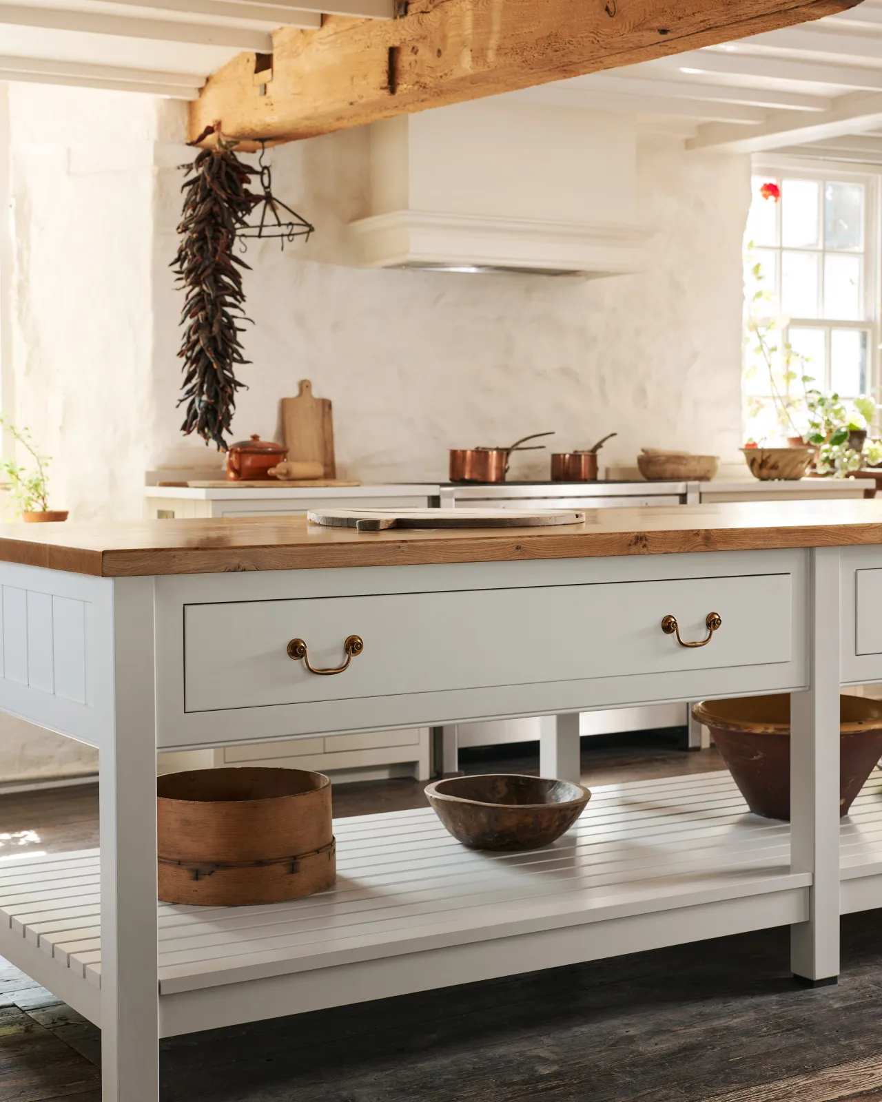 Two Georgian-style brass swing handles on a light-coloured Shaker-style kitchen prep table with a warm oak worktop.