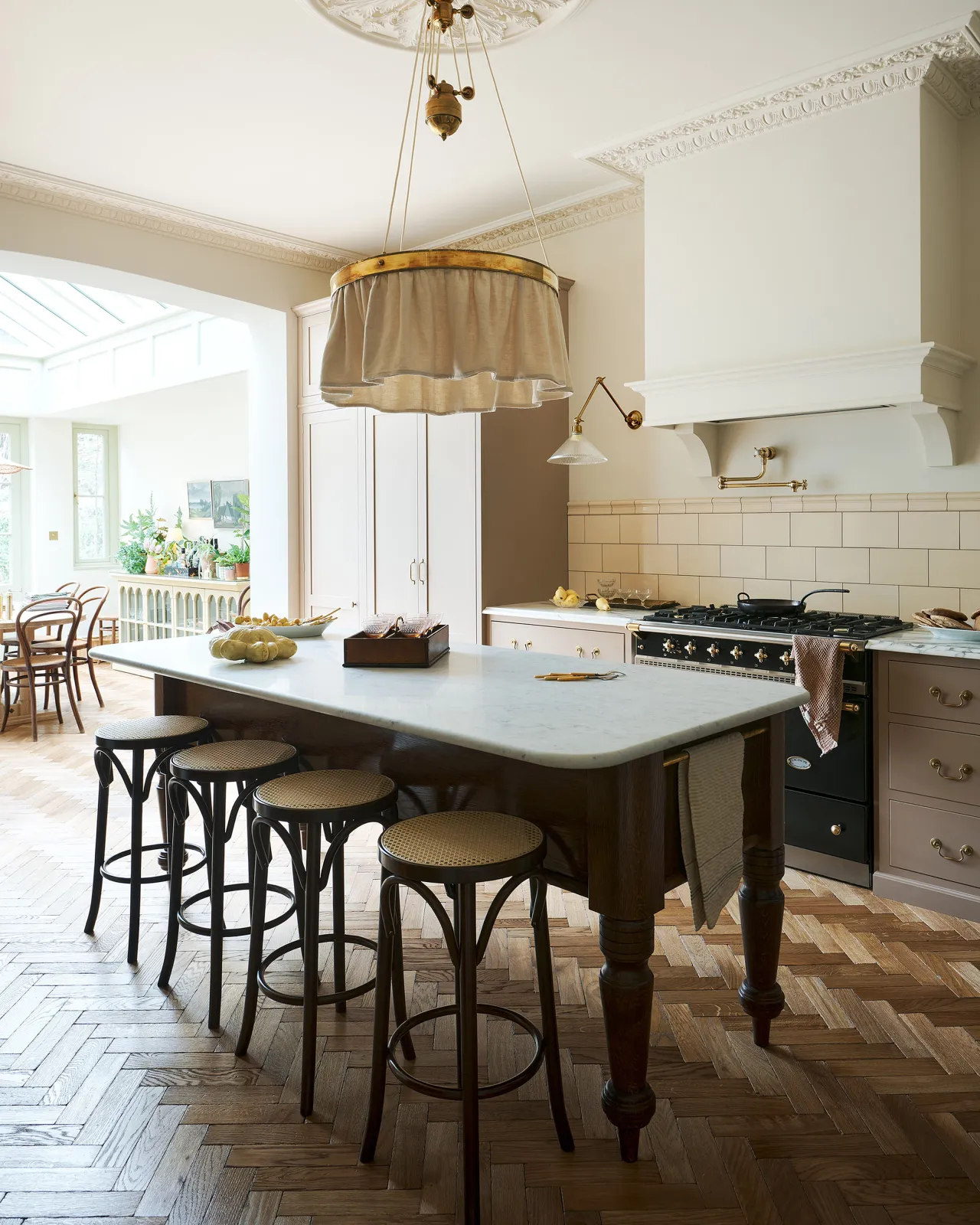 An oblique view of a grand oak prep table with a Carrara marble worktop with a row of café-style bar stools with dark stained frames and light woven ratten seats.