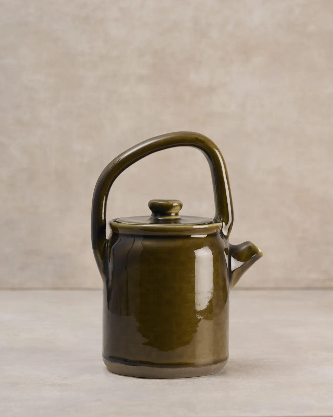 A side profile view of a small mid-century-style ceramic teapot with a glossy amber glaze.
