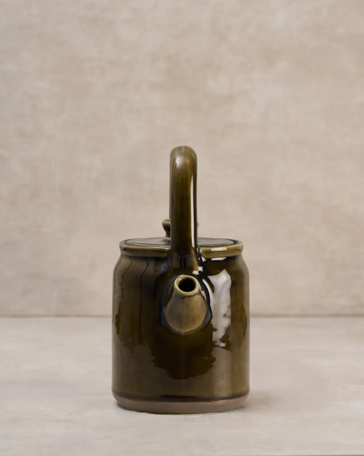 A front profile view of a small mid-century-style ceramic teapot with a glossy amber glaze.