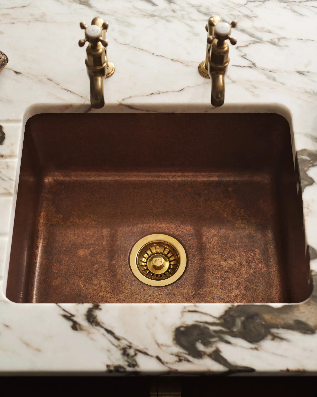 Overhead view of the copper single sink with a patinated finish and brass fittings, set in a white marble worktop with dark veining.
