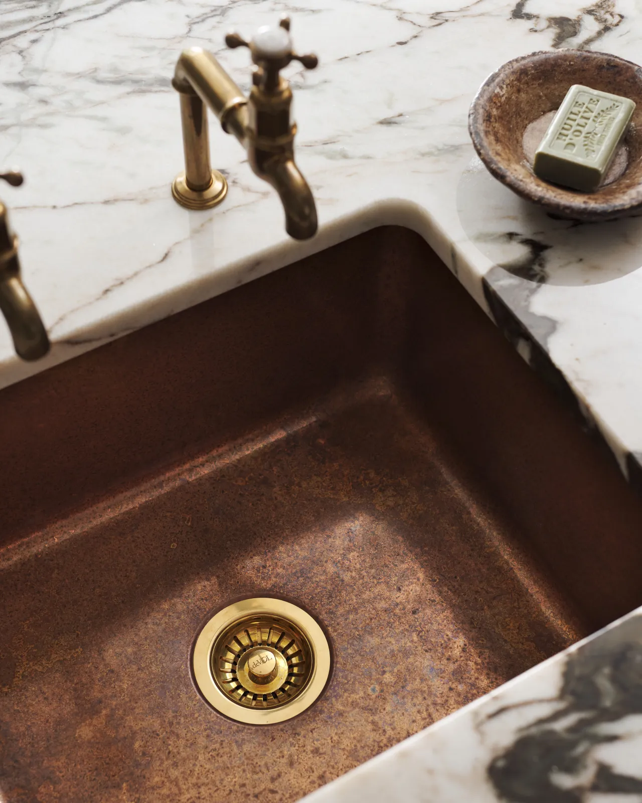 Close-up of the copper single sink corner with a vintage-style soap dish and brass taps on a marble counter.