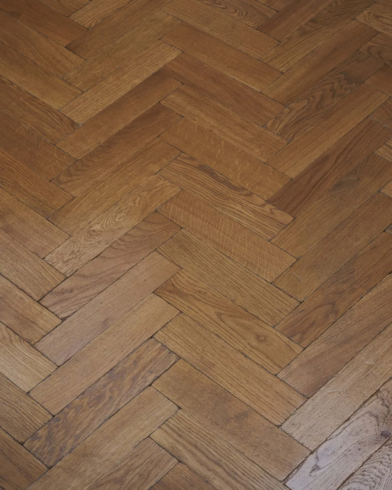 A close-up overhead view of oak parquet flooring with a warm aged finish.