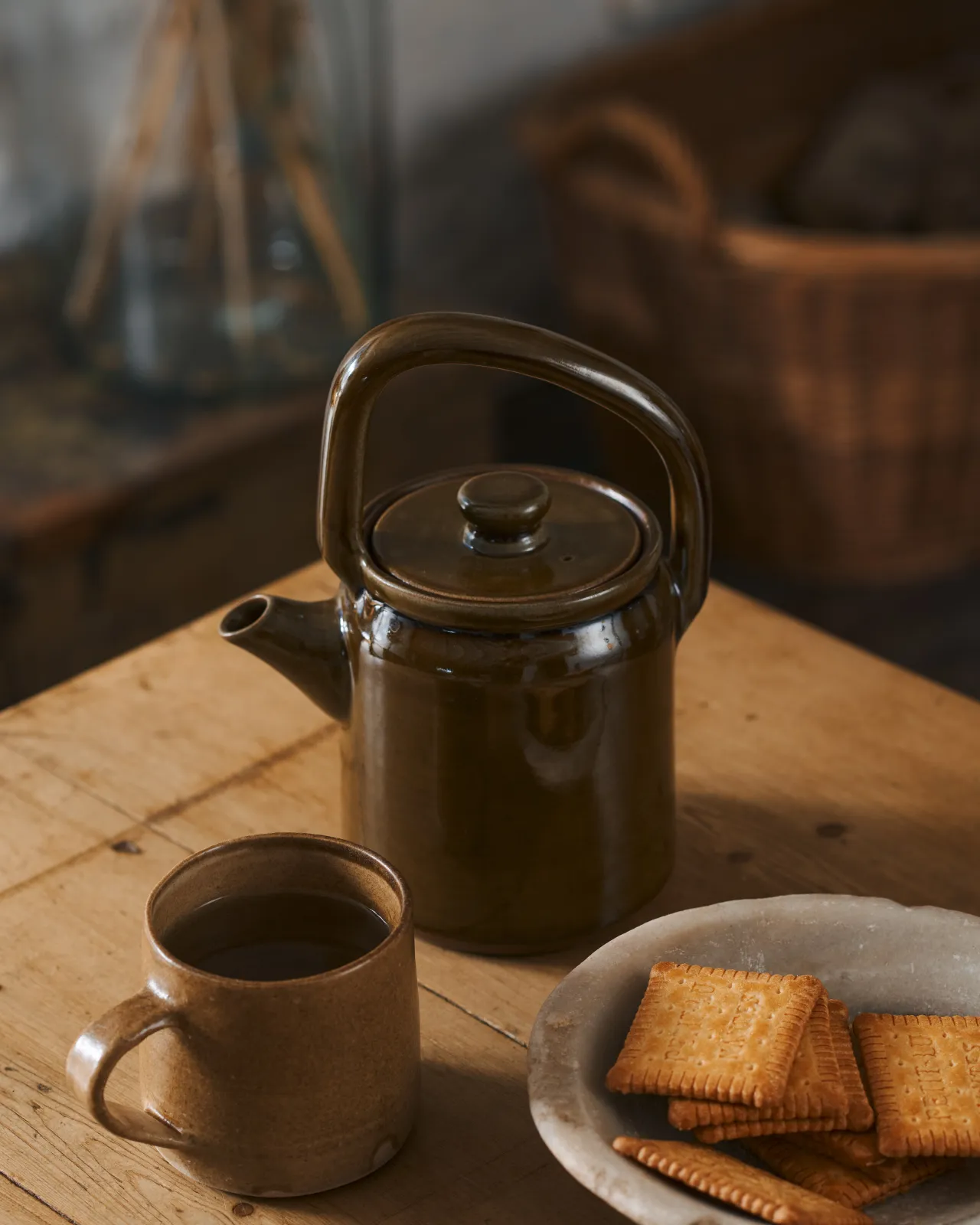 Amber glaze teapot on a wooden table with biscuits on the side.