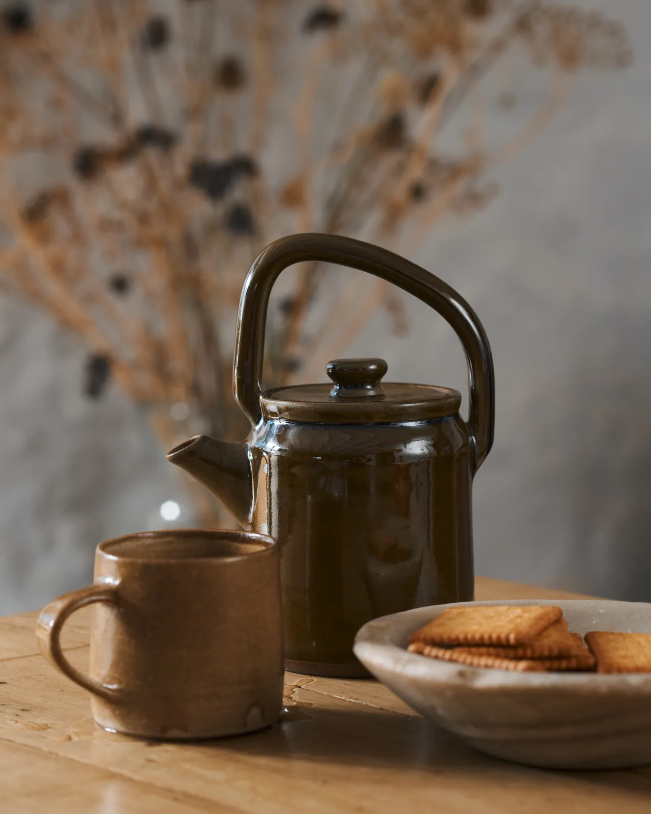 Amber glaze teapot on a wooden table with biscuits on the side.