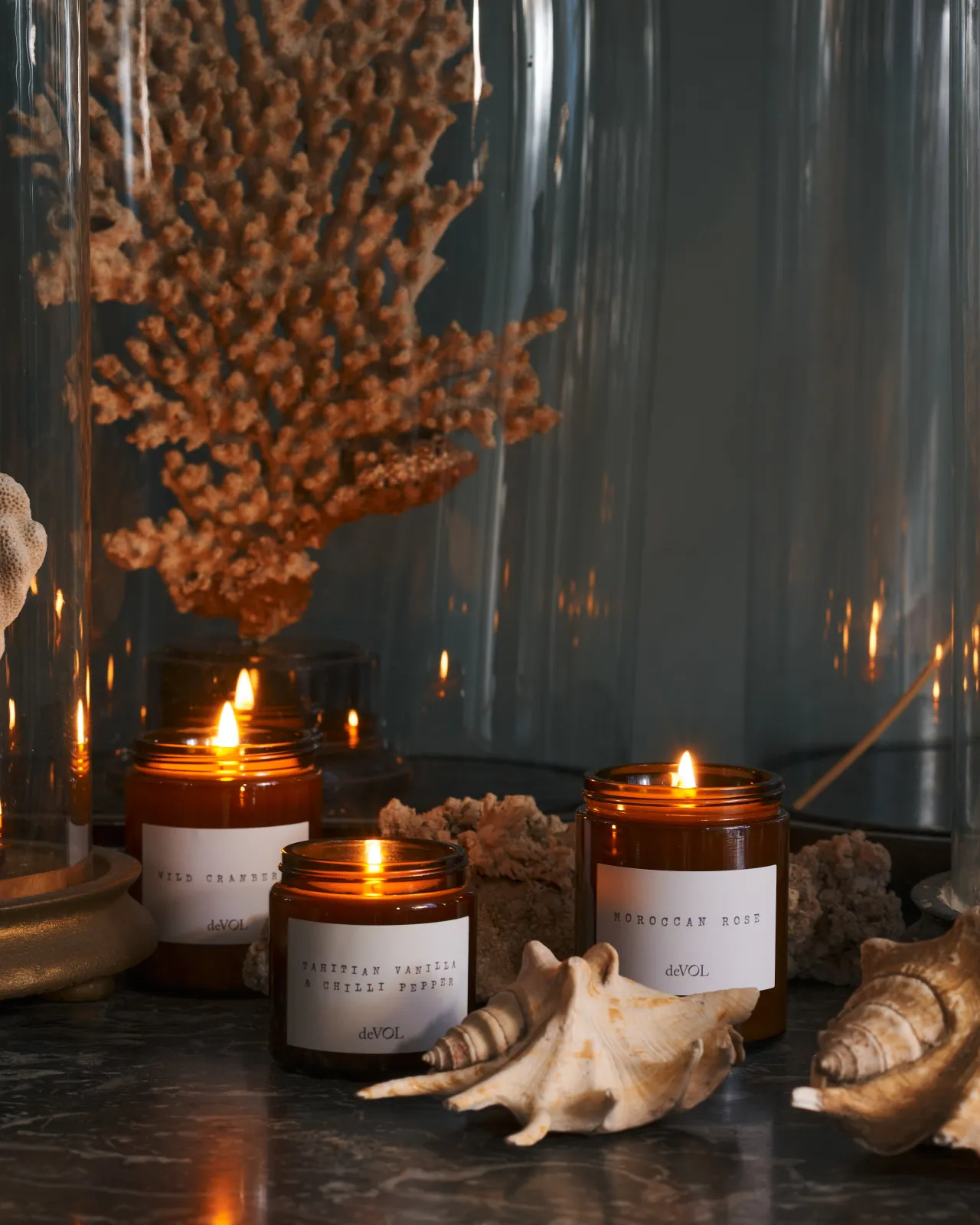 a front on shot of the small and medium candle surrounded by dried sea shells on a black stone top dresser.