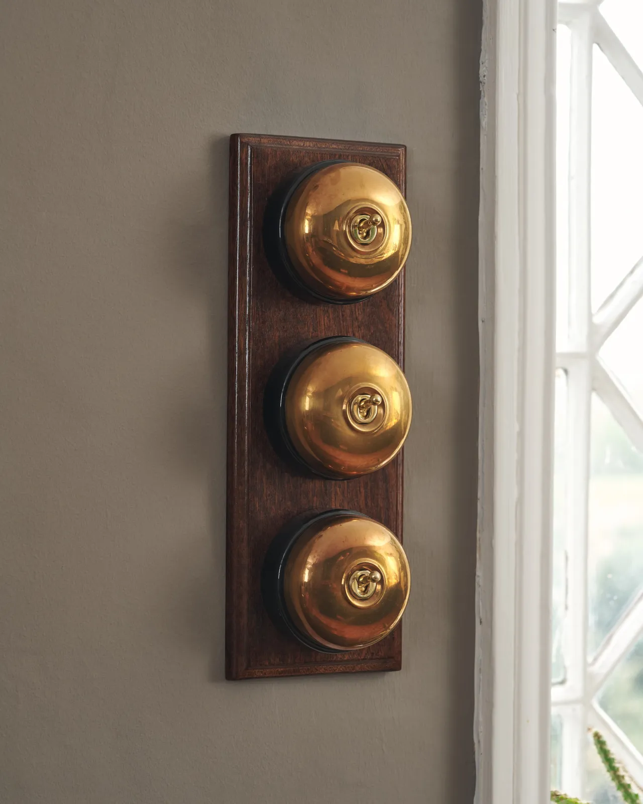 Three Heirloom Brass deVOL Dolly Toggle Switches fitted to a stained sapele pattress.