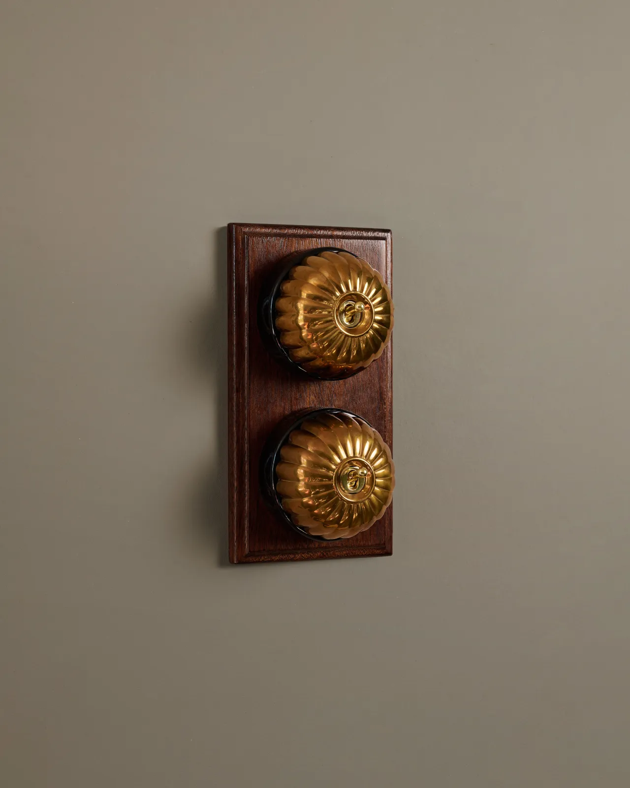 A pair of deVOL Jelly Toggle Switches in Heirloom Brass and fitted to a richly stained Sapele pattress.