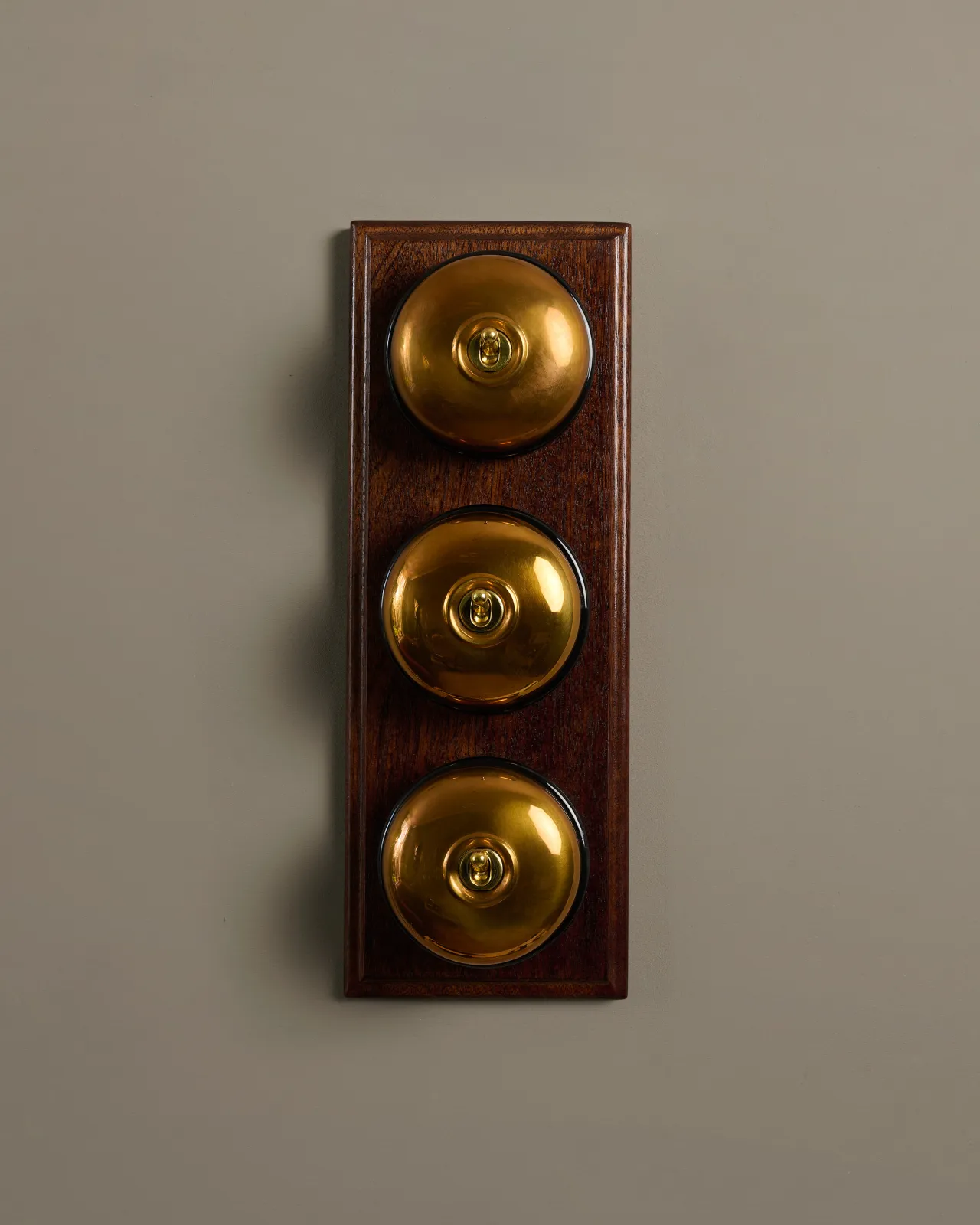 A row of three deVOL Heirloom Brass Dolly Toggle Switches fitted to a Mahogany Finish pattress. 