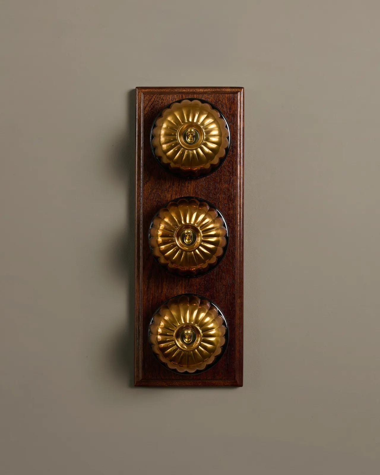 A row of three deVOL Heirloom Brass Jelly Toggle Switches fitted to a Mahogany Finish pattress.
