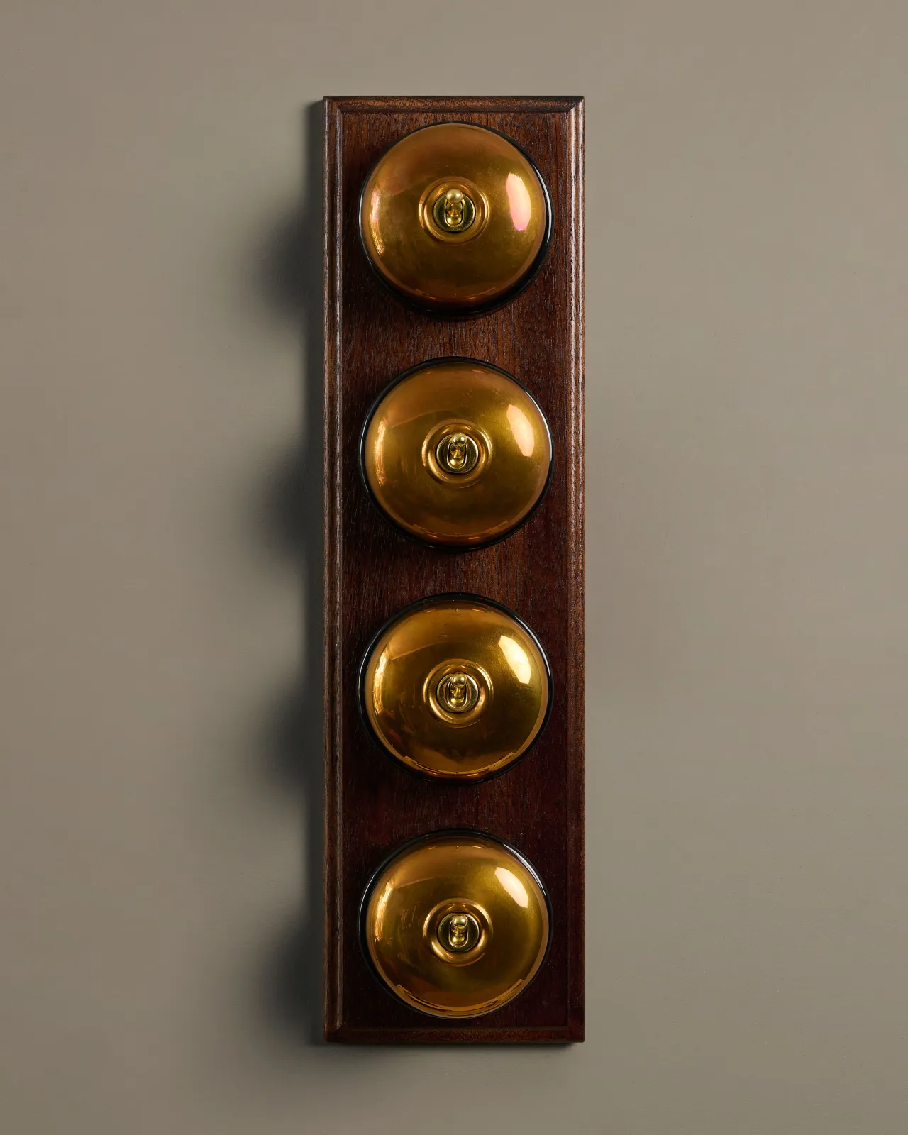 A row of four deVOL Heirloom Brass Dolly Toggle Switches fitted to a Mahogany Finish pattress.