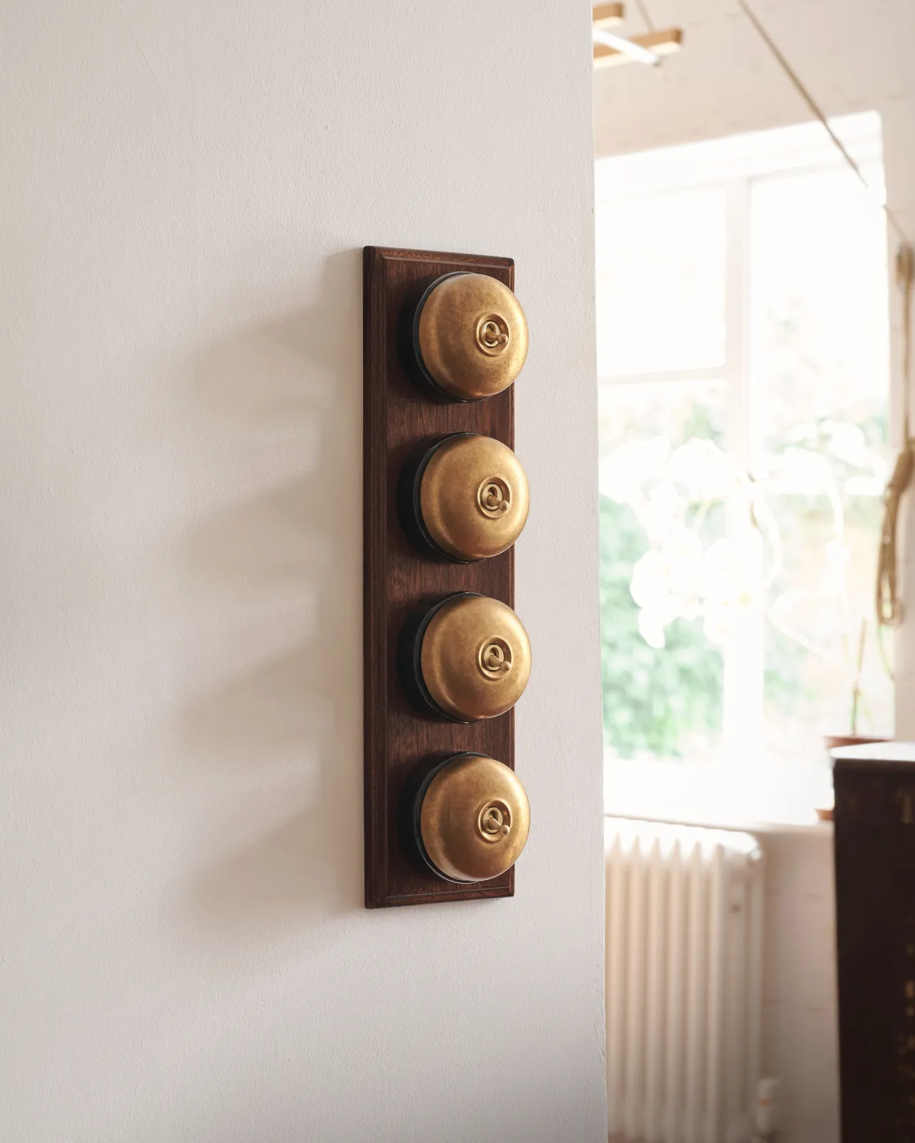 A bank of four Aged Brass Dolly Toggle Switches fitted to a richly stained Sapele pattress. Photographed in a light and airy scullery.