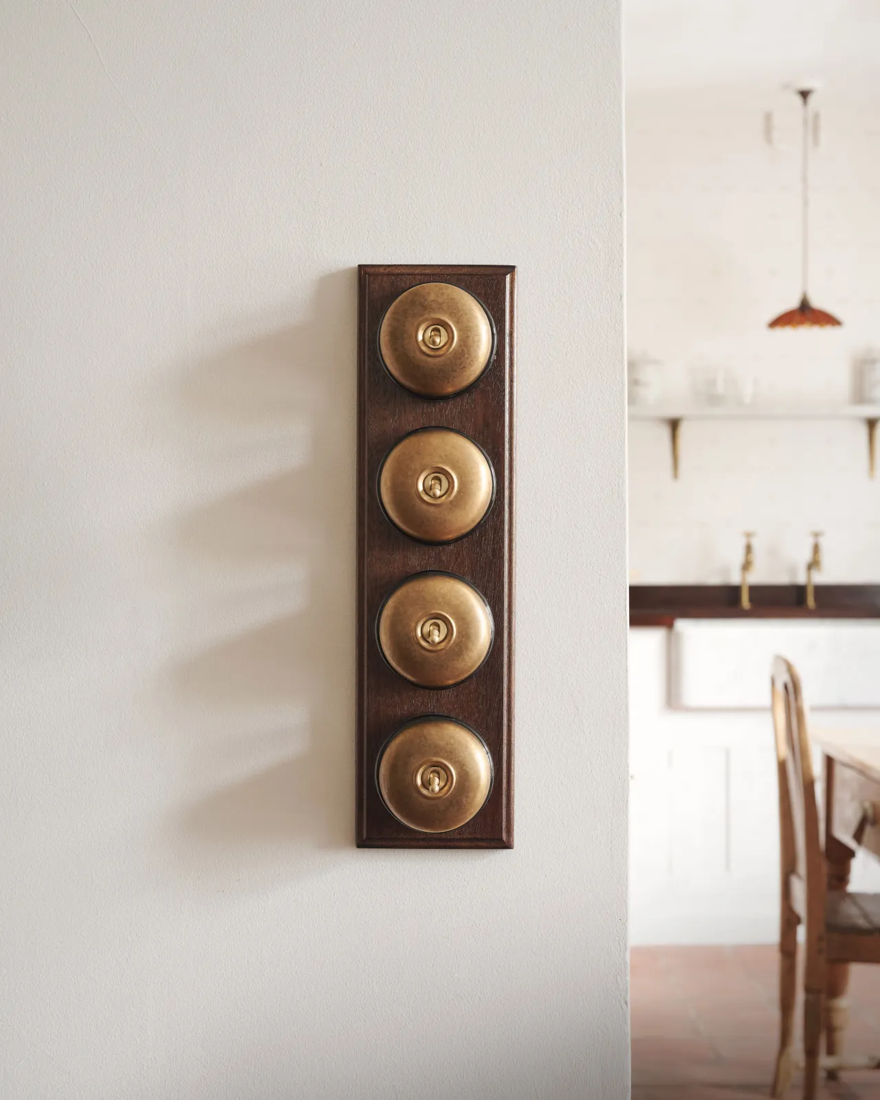 A bank of four Aged Brass Dolly Toggle Switches fitted to a richly stained Sapele pattress. Photographed in a light and airy scullery.