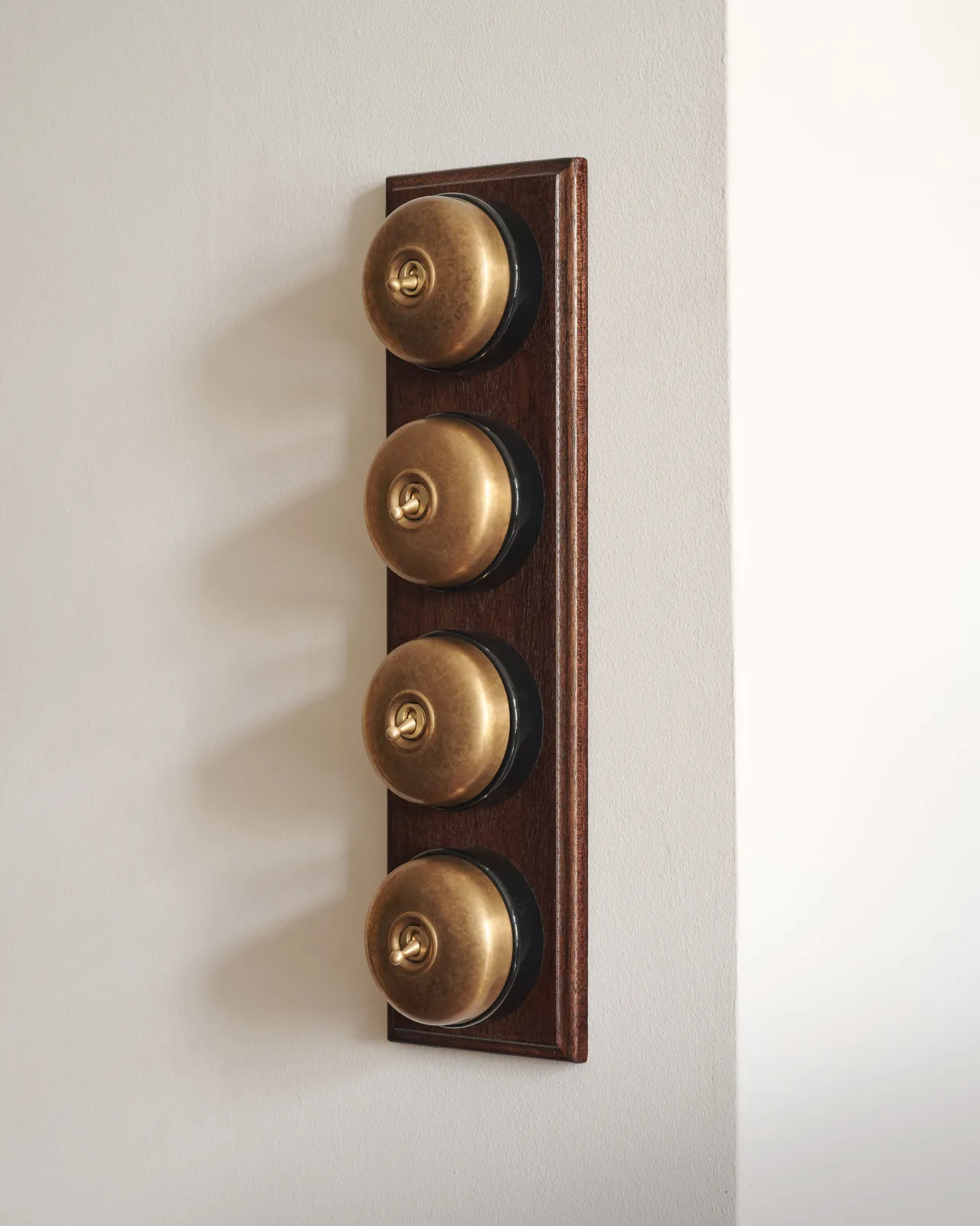 A bank of four Aged Brass Dolly Toggle Switches fitted to a richly stained Sapele pattress. Photographed in a light and airy scullery.