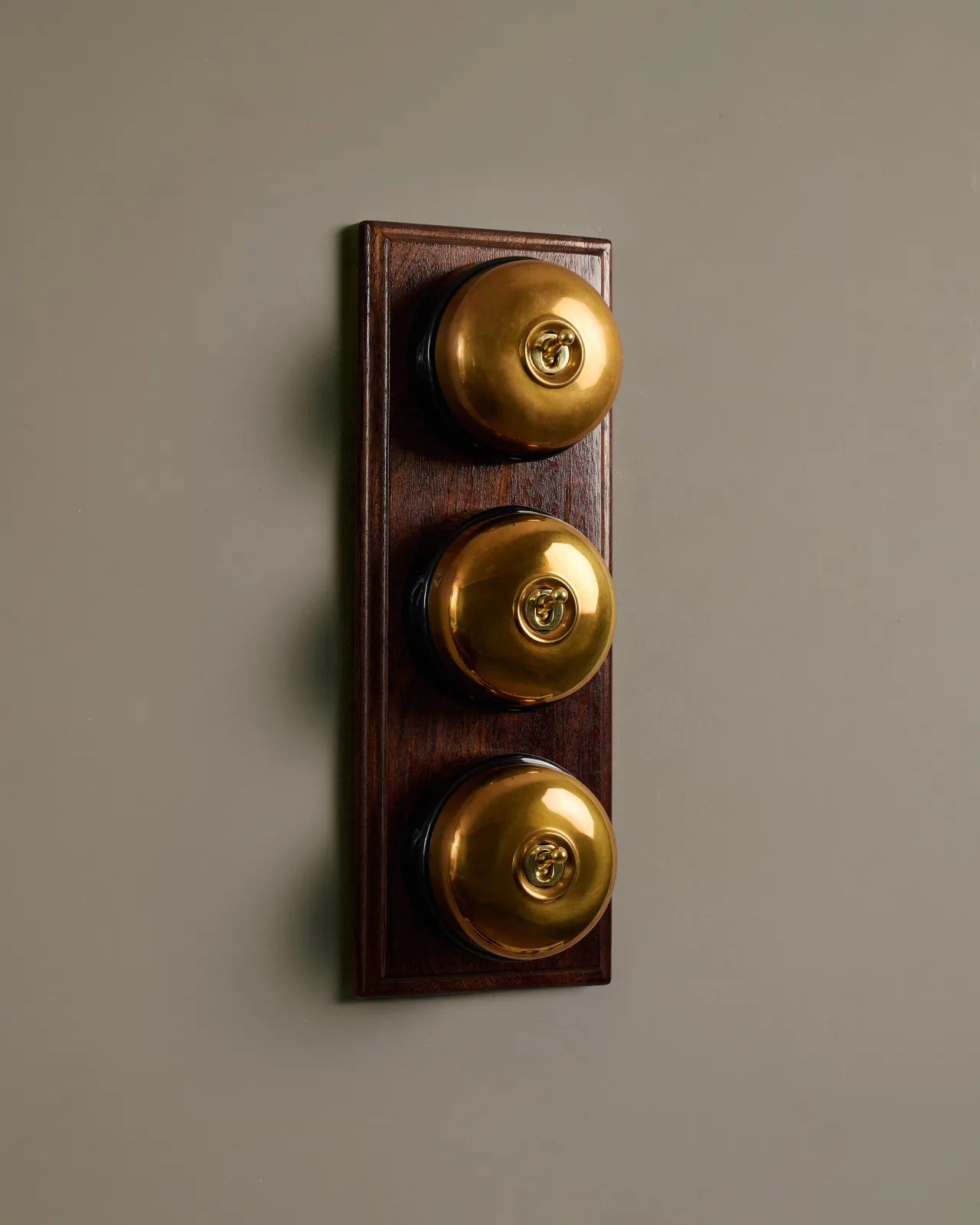 A row of three deVOL Heirloom Brass Dolly Toggle Switches fitted to a Mahogany Finish pattress.