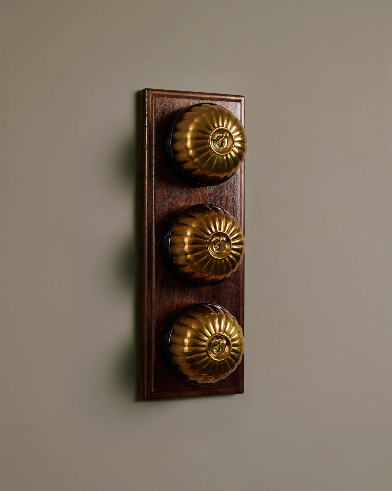 A row of three deVOL Heirloom Brass Jelly Toggle Switches fitted to a Mahogany Finish pattress.