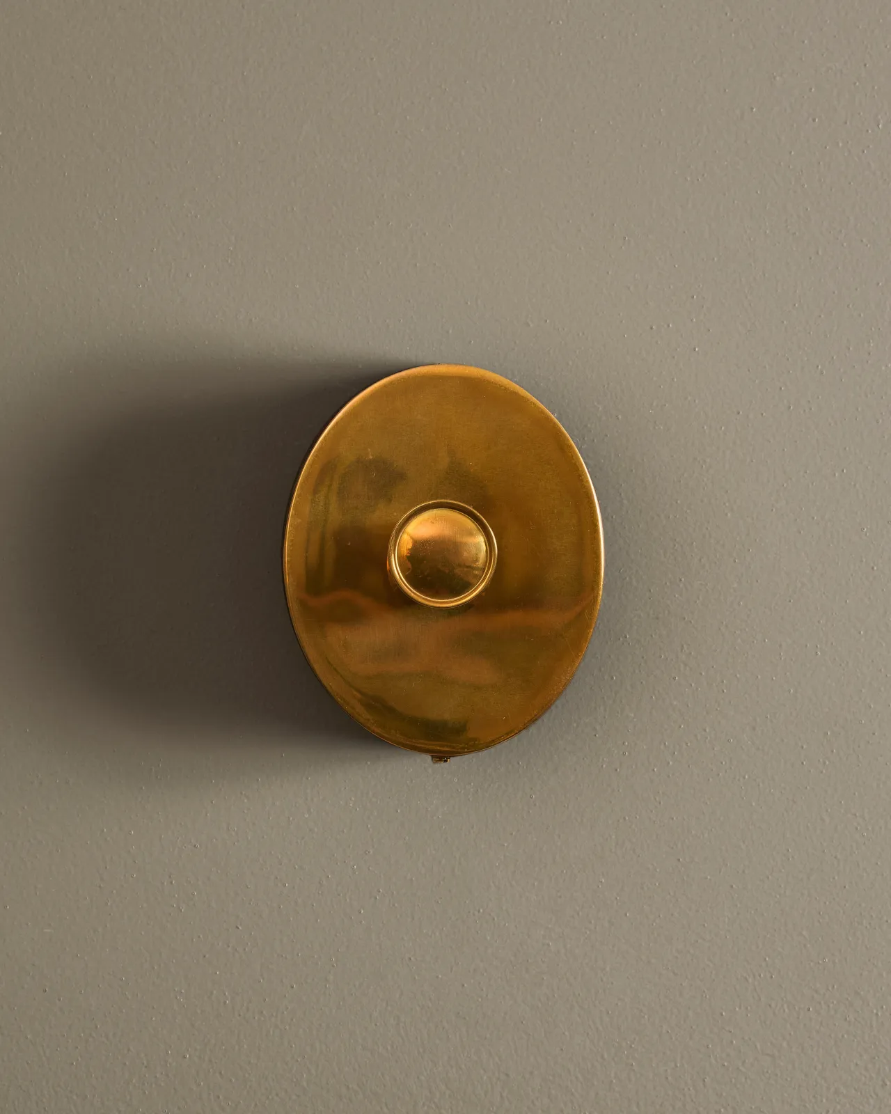 A straight-on view of a small 1 gang oval-shaped dimmer switch in a warm burnished brass finish with a black base.