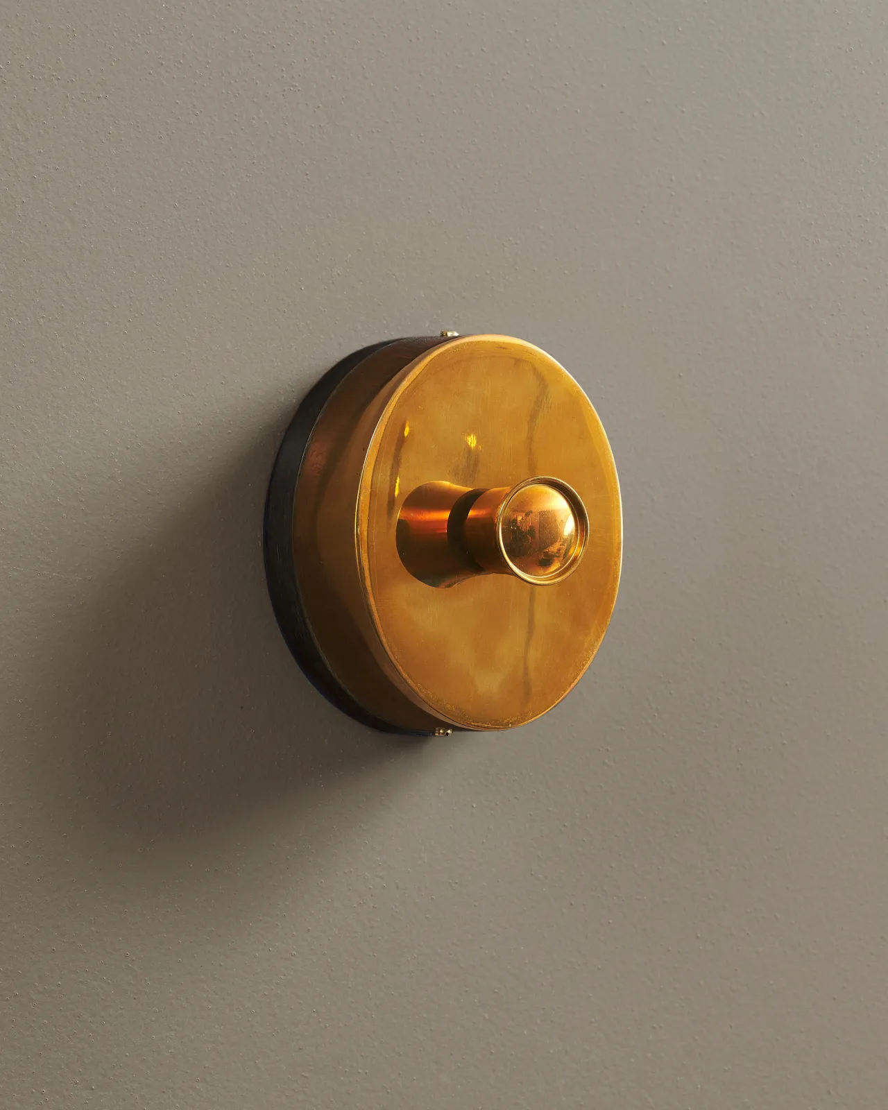 An oblique view of a small 1 gang oval-shaped dimmer switch in a warm burnished brass finish with a black base.