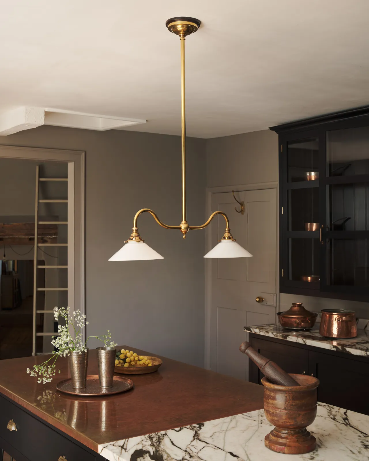 An elegant ceiling light with a rigid brass pole and two curved arms, each holding a small milk glass shade.