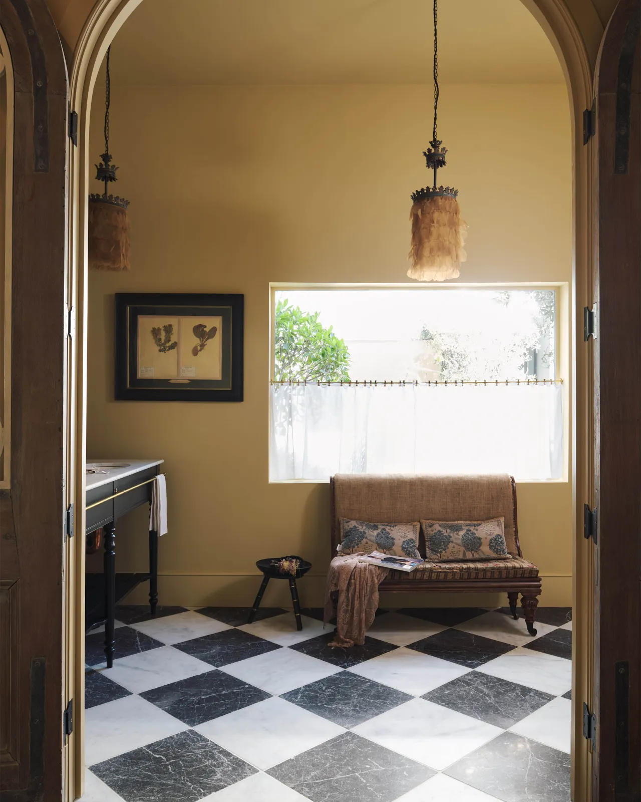 Looking through an archway into a yellow room with a black and white chequered marble floor and a small vintage sofa.