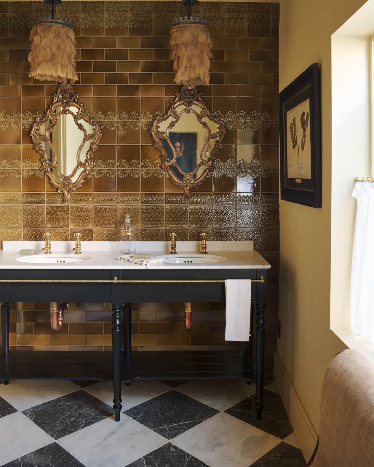 A black and white chequered marble floor with a classic black twin washstand with brass fittings and a wall of lace-patterned glossy sepia tiles.