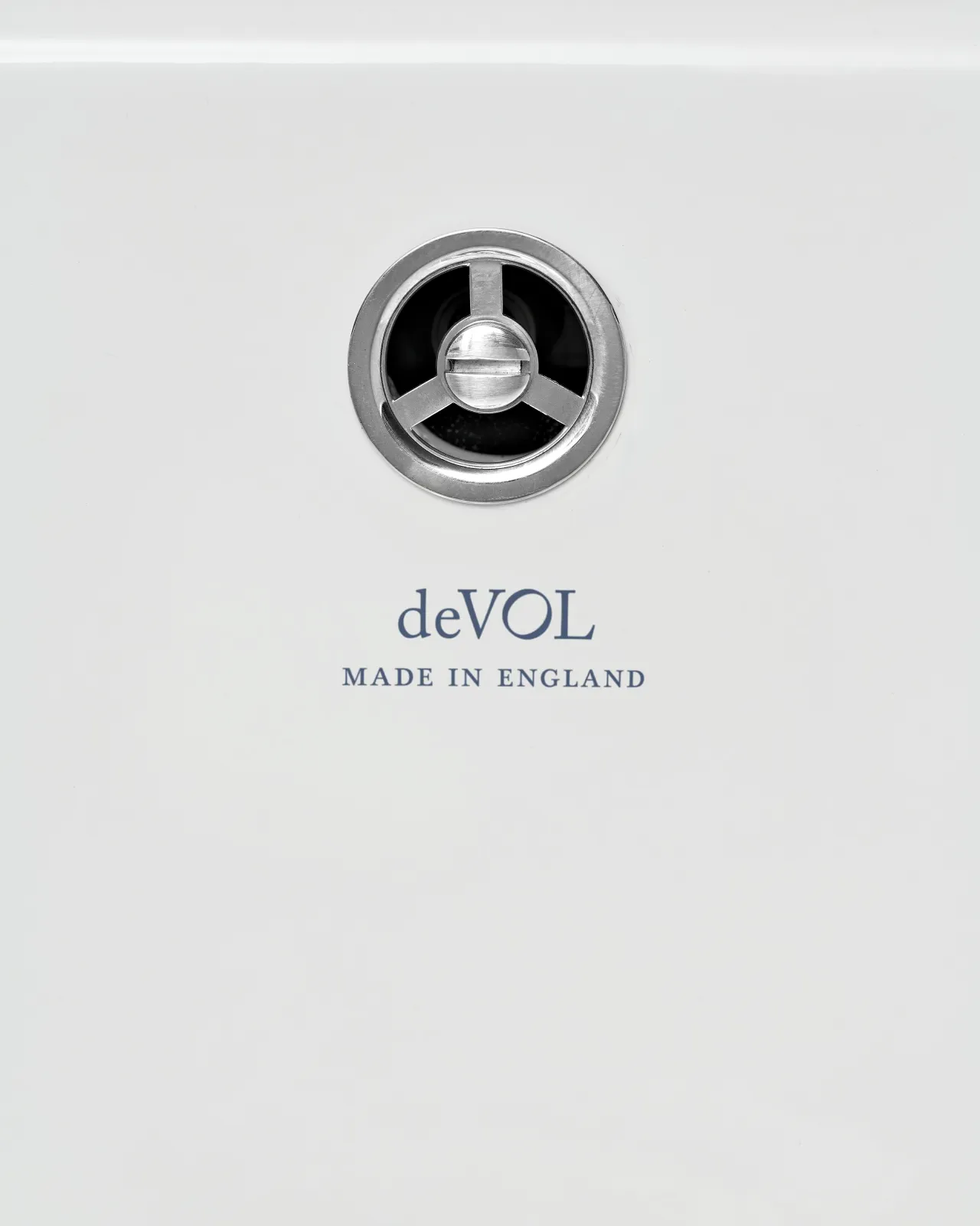 A round sink overflow cap in a chrome finish, fitted to a ceramic sink with the words 'deVOL, Made in England' printed in the glaze below.